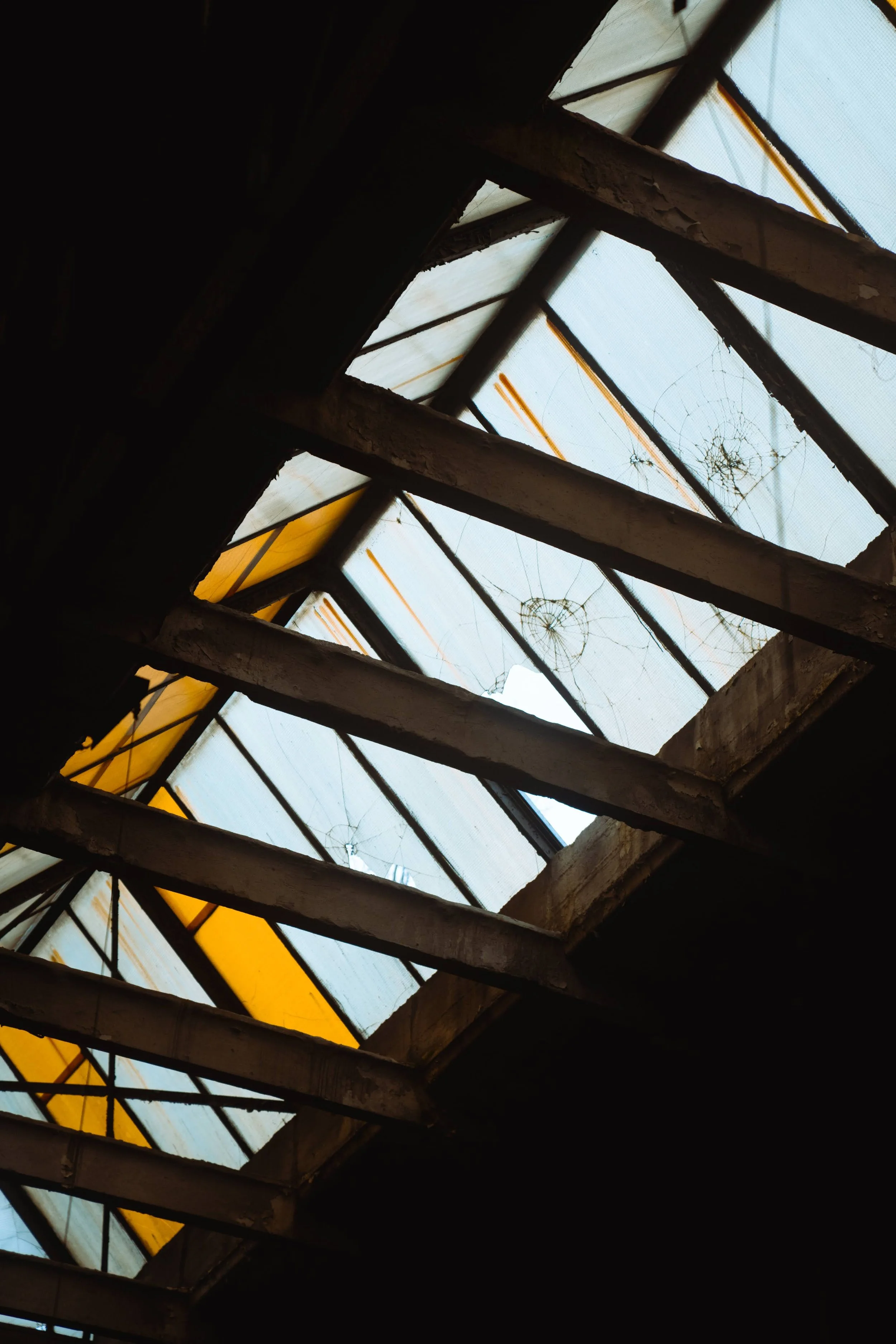 Looking up through a broken, weathered ceiling with spider webs in the skylight.