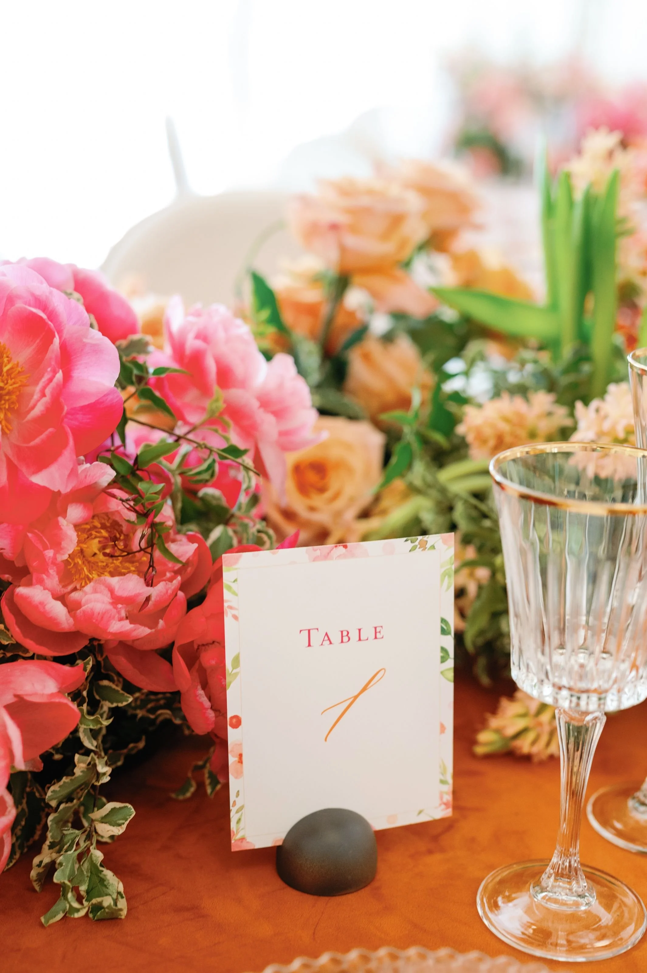 A wedding table centerpiece with pink and peach flowers, a table number card, and glassware. Crystal Plaza Livingston, NJ 