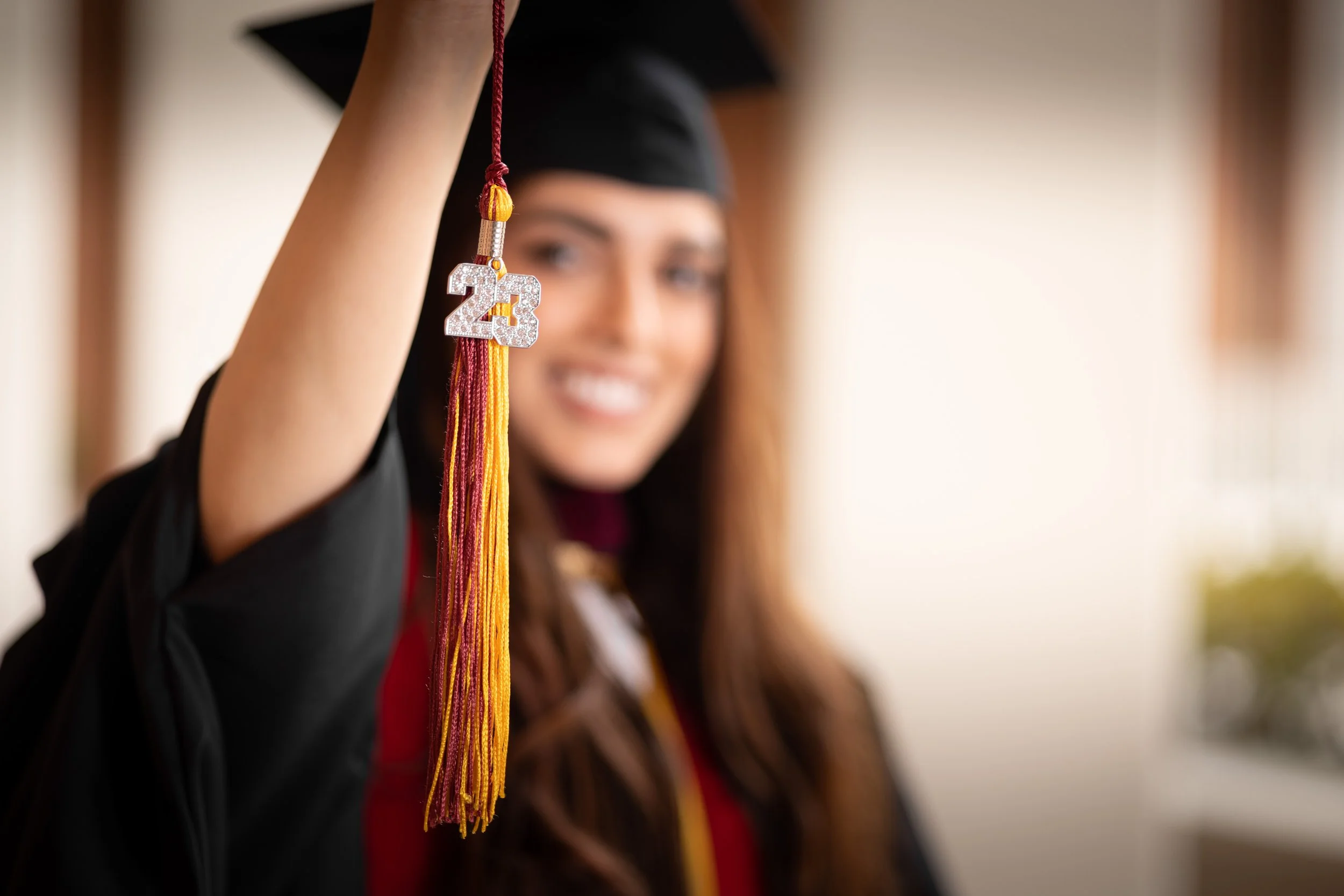 Graduation cap and gown with a tassel featuring the number 23, worn by a smiling graduate.