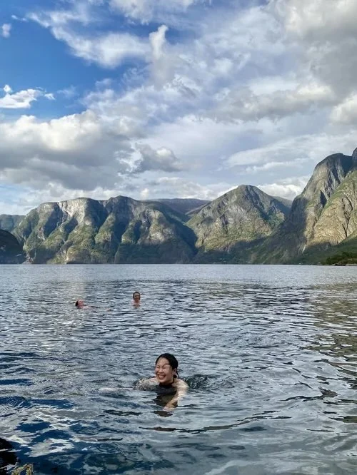 To personer som svømmer i en innsjø omgitt av fjell under en skyet himmel.