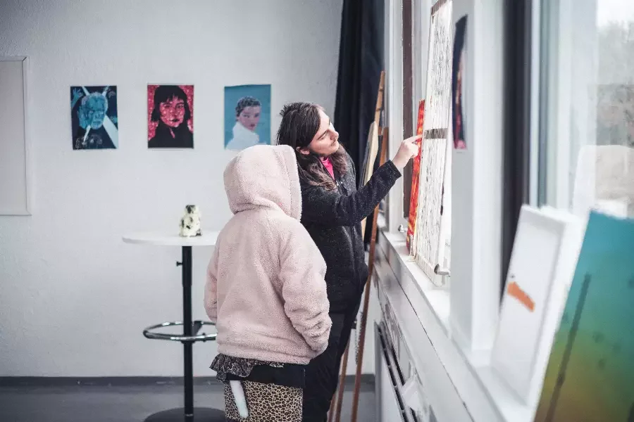 En kvinne og et barn ser på malerier i et galleri, kvinnen peker på et av maleriene.