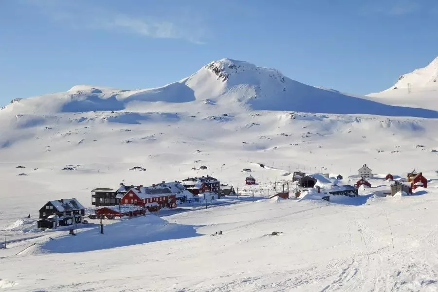 Snødekte fjell og en liten landsby med hus i varierende farger.