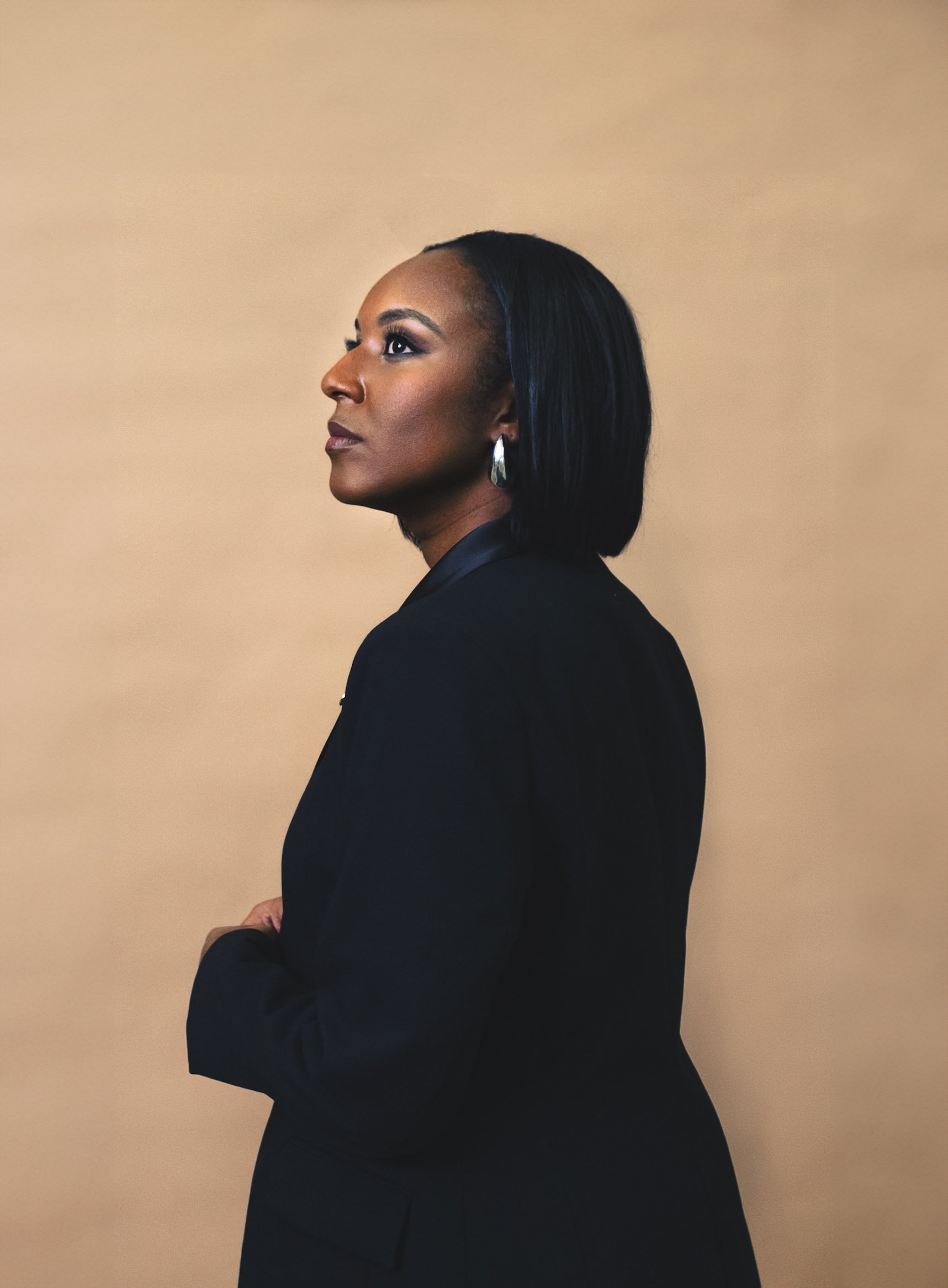 Portrait of a person wearing a black jacket, looking to the side, with a neutral beige background.