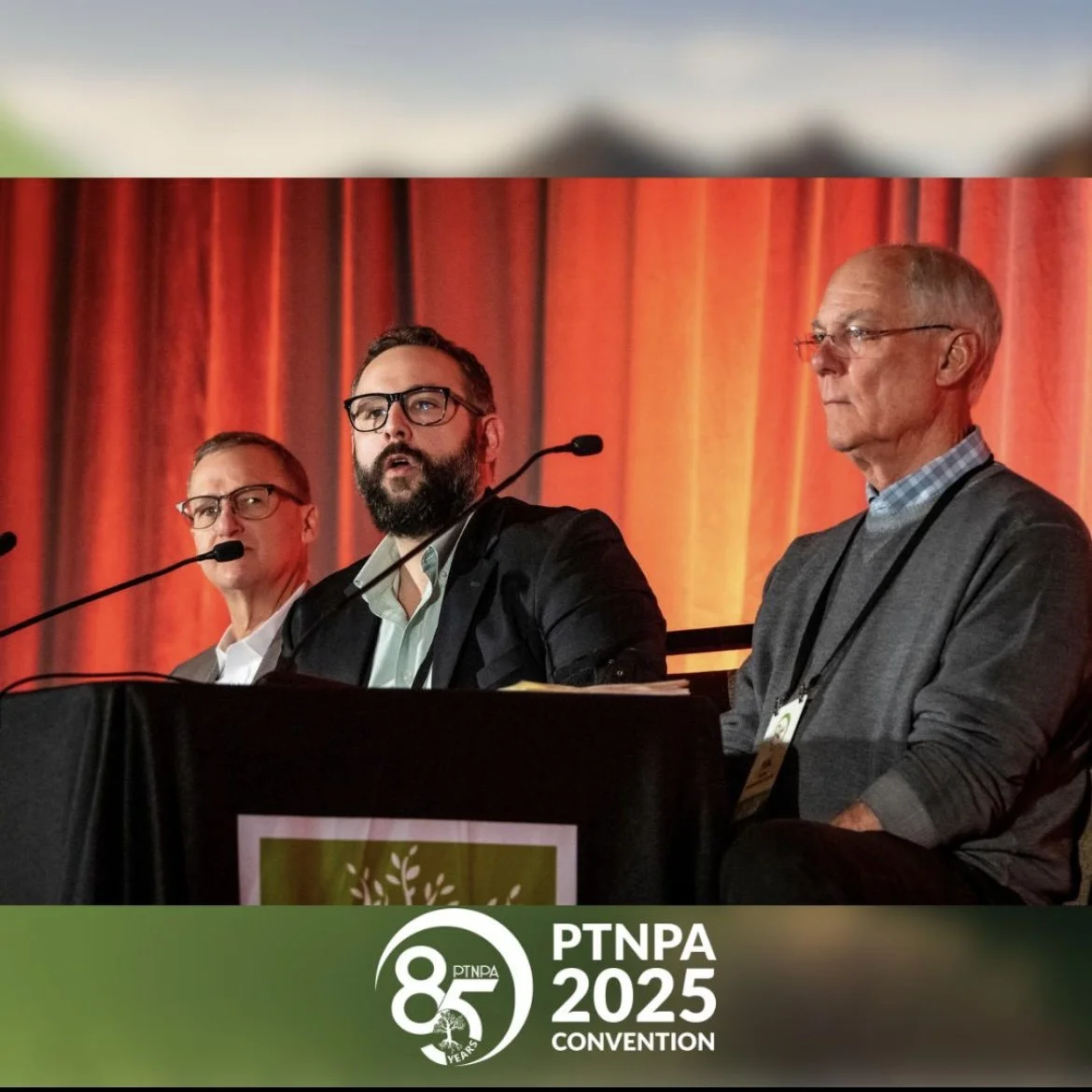 Three men speaking at a conference table with microphones, orange curtains in the background, and a black tablecloth with a PTNPA 85th anniversary logo and 2025 convention sign.