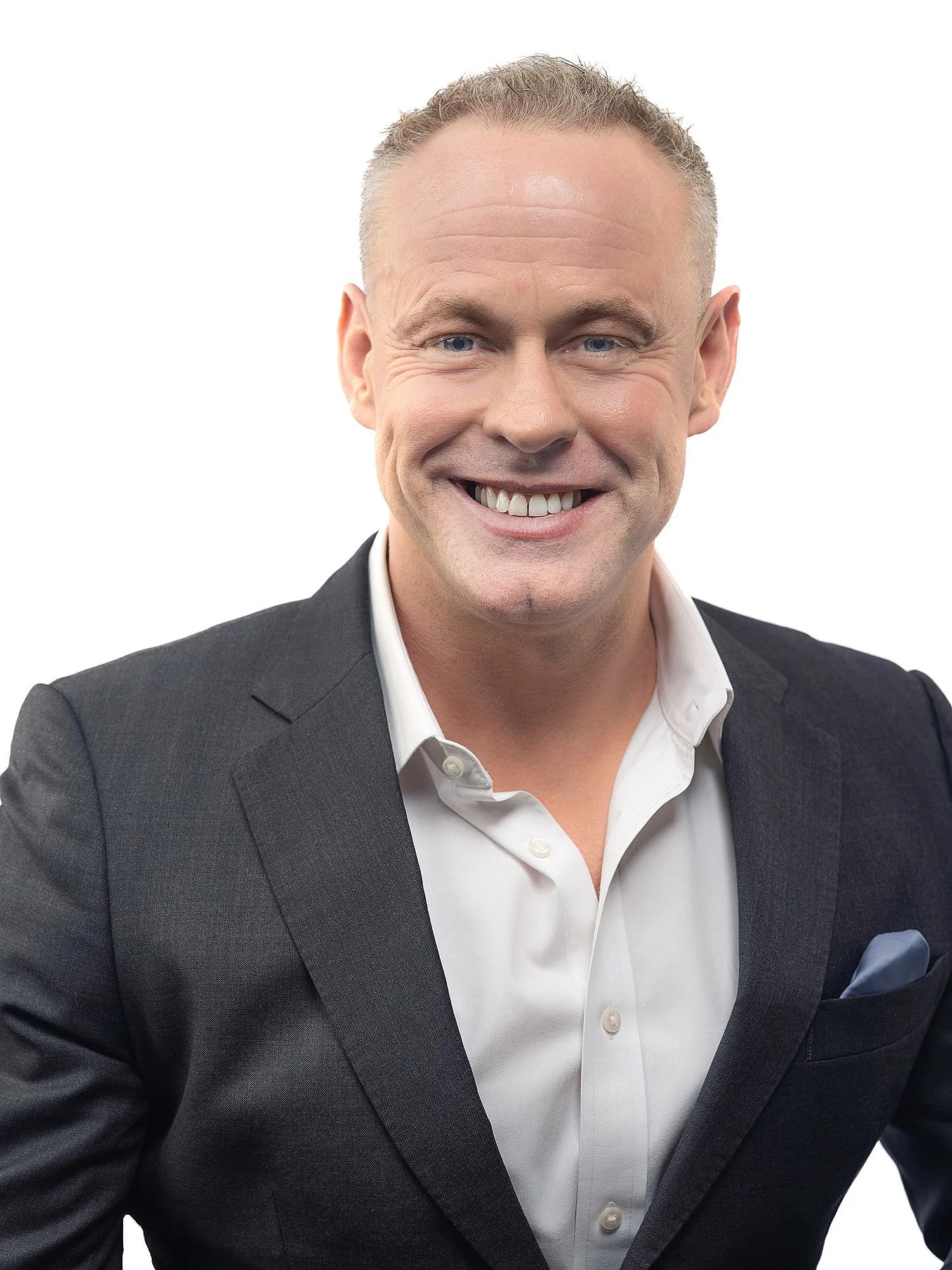 A smiling man with short blonde hair, blue eyes, wearing a dark suit jacket and white shirt, against a plain white background.