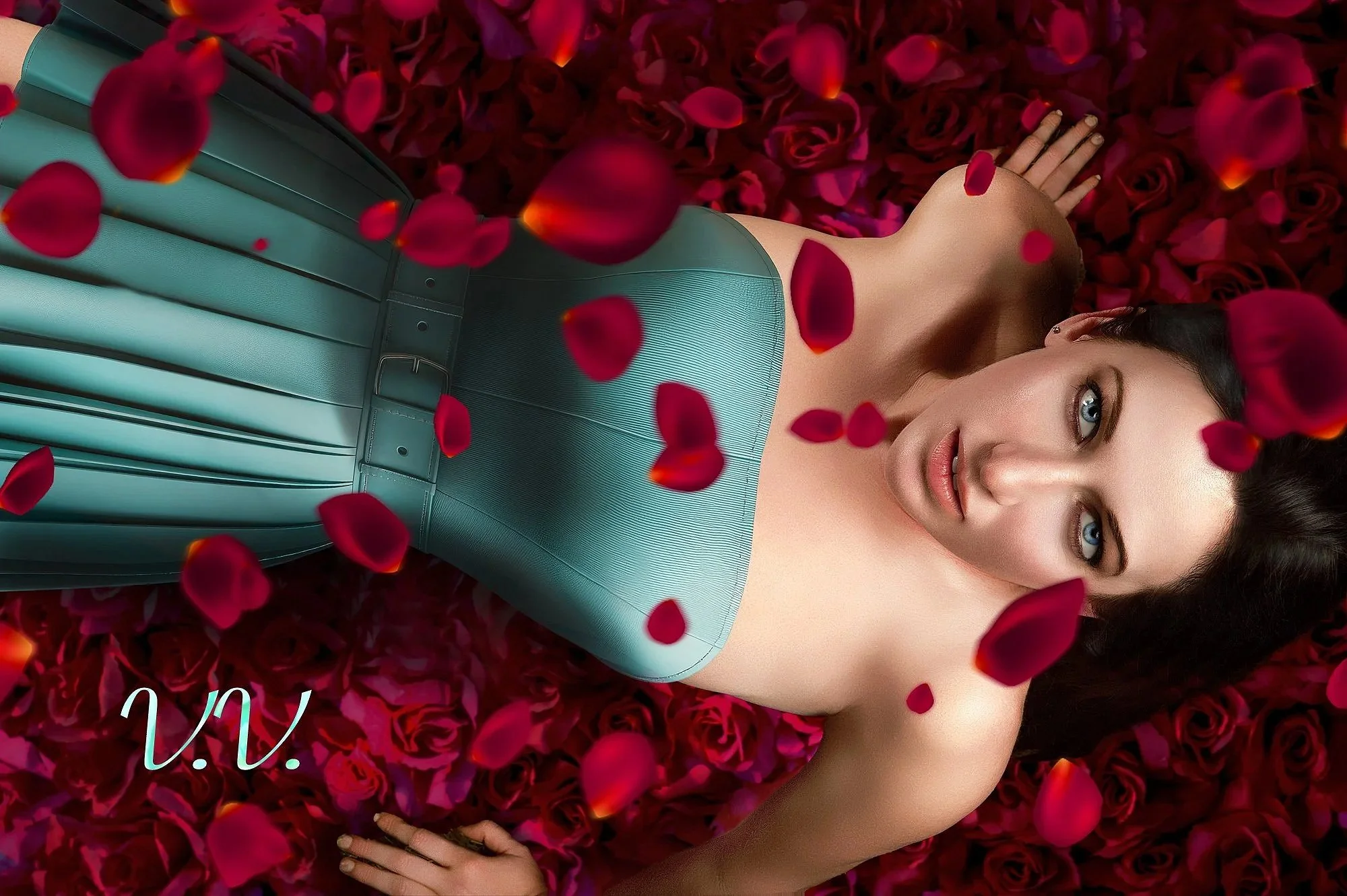 A woman with blue eyes lying on a bed of red rose petals, wearing a teal strapless dress, with rose petals falling around her.