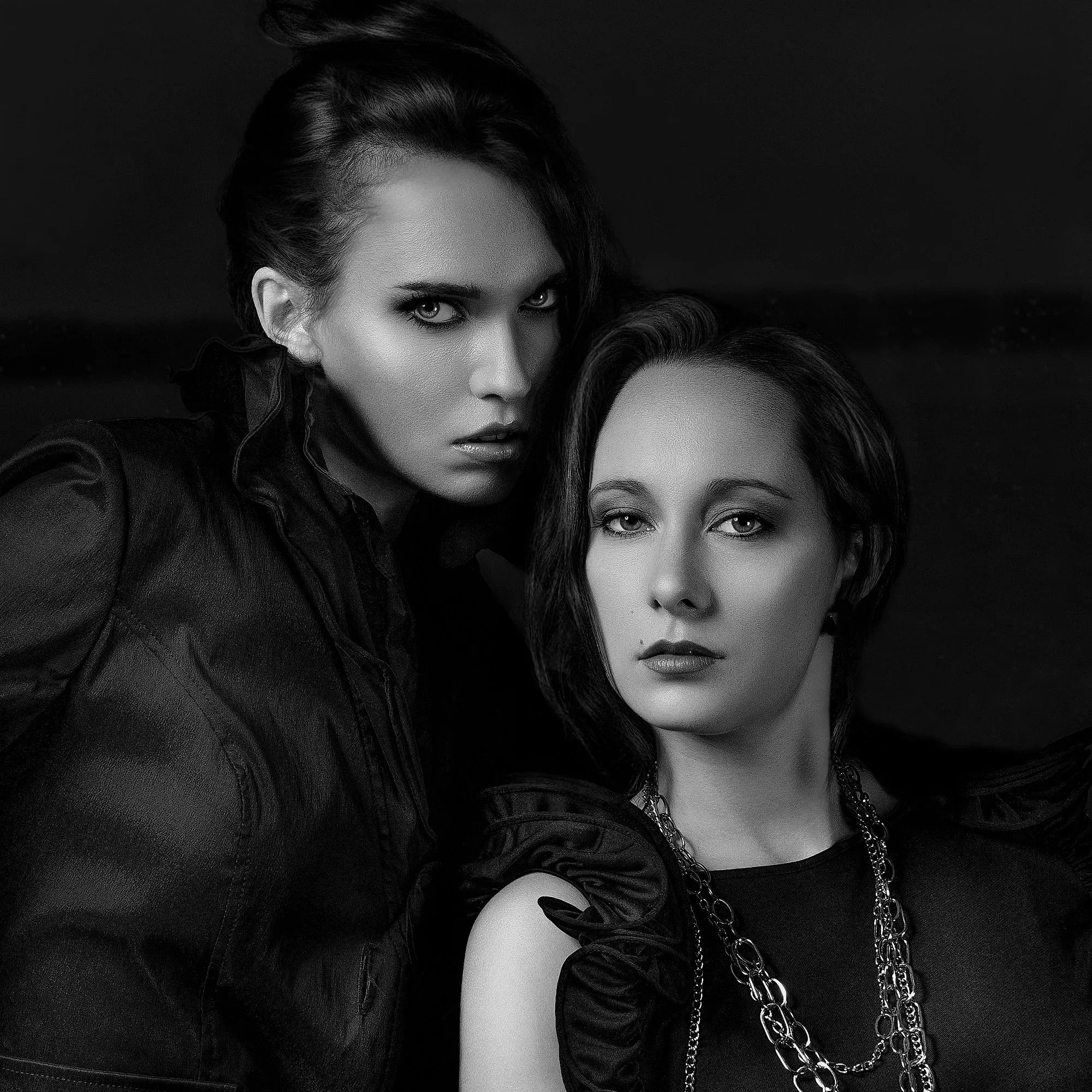 Two women with dark hair and intense expressions, wearing dark clothing, posing closely together in a black and white photo. Best-Fashion-Portrait-Commercial-Business-Headshots-Corporate- photography-Maryland-Washington D.C.-Pennsylvania-Virginia