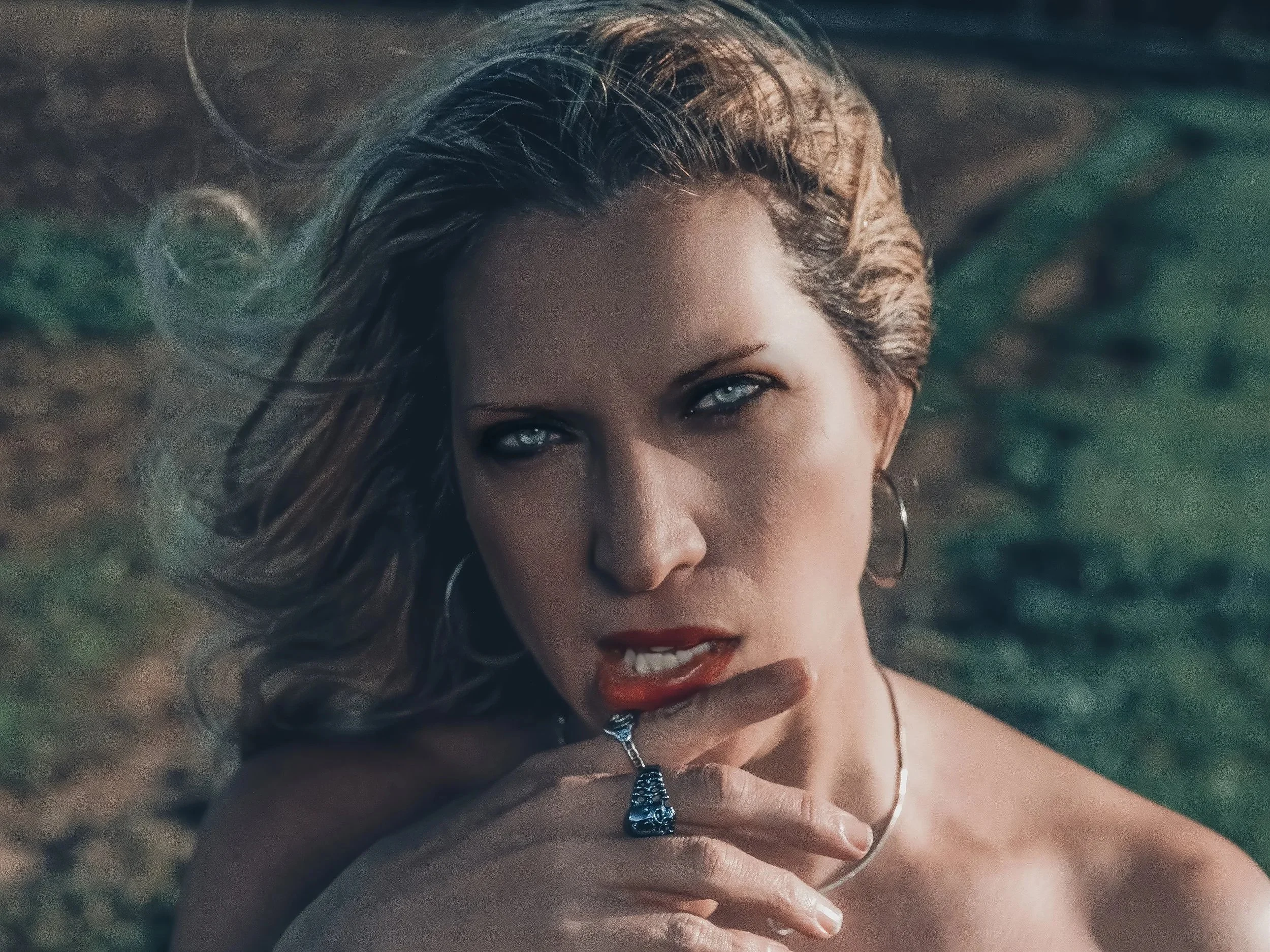 Close-up of a woman with wavy blonde hair, blue eyes, wearing hoop earrings, a necklace, and a ring, with her hand near her lips, outdoors in natural light. Best-Fashion-Portrait-Commercial-Business-Headshots-Corporate- photography-Maryland-Washingto