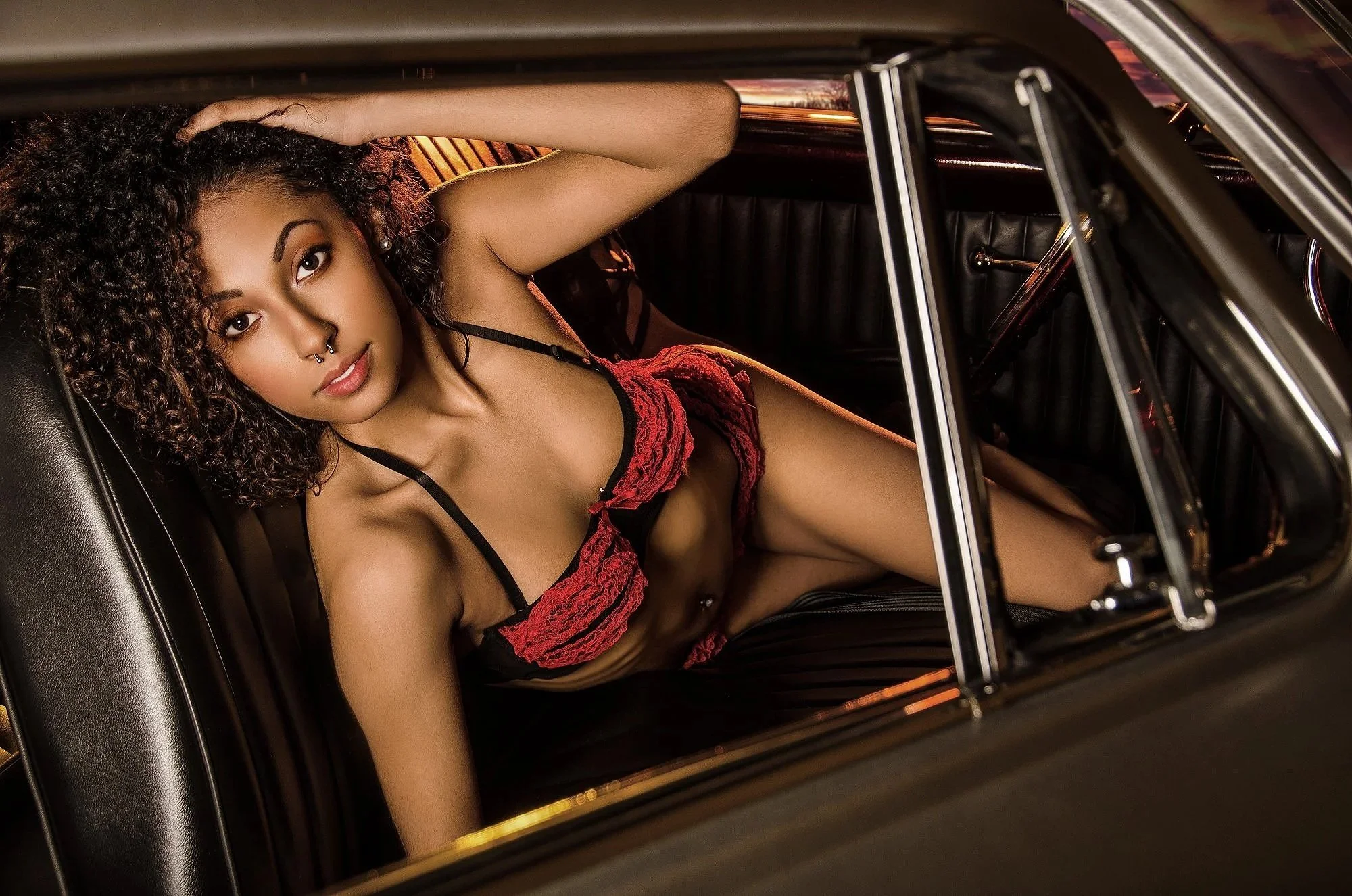 A young woman with curly hair, wearing red lingerie with black straps, sitting in the back seat of a car, looking at the camera. Best-Fashion-Portrait-Commercial-Business-Headshots-Corporate- photography-Maryland-Washington D.C.-Pennsylvania-Virginia