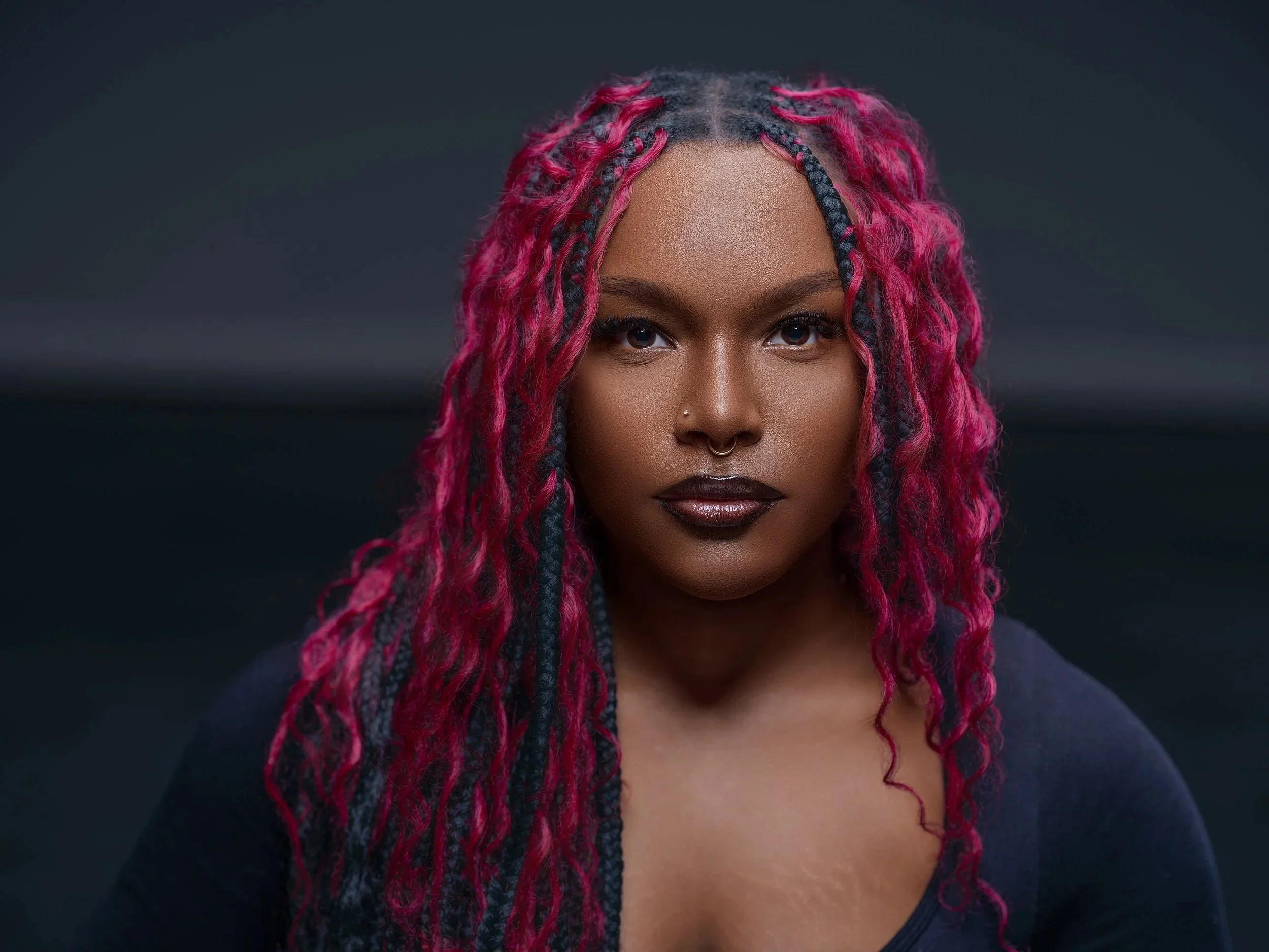 Portrait of a woman with dark skin and pink and black box braids, wearing dark lipstick and a nose ring, against a dark background. Best-Fashion-Portrait-Commercial-Business-Headshots-Corporate- photography-Maryland-Washington D.C.-Pennsylvania-Virgi