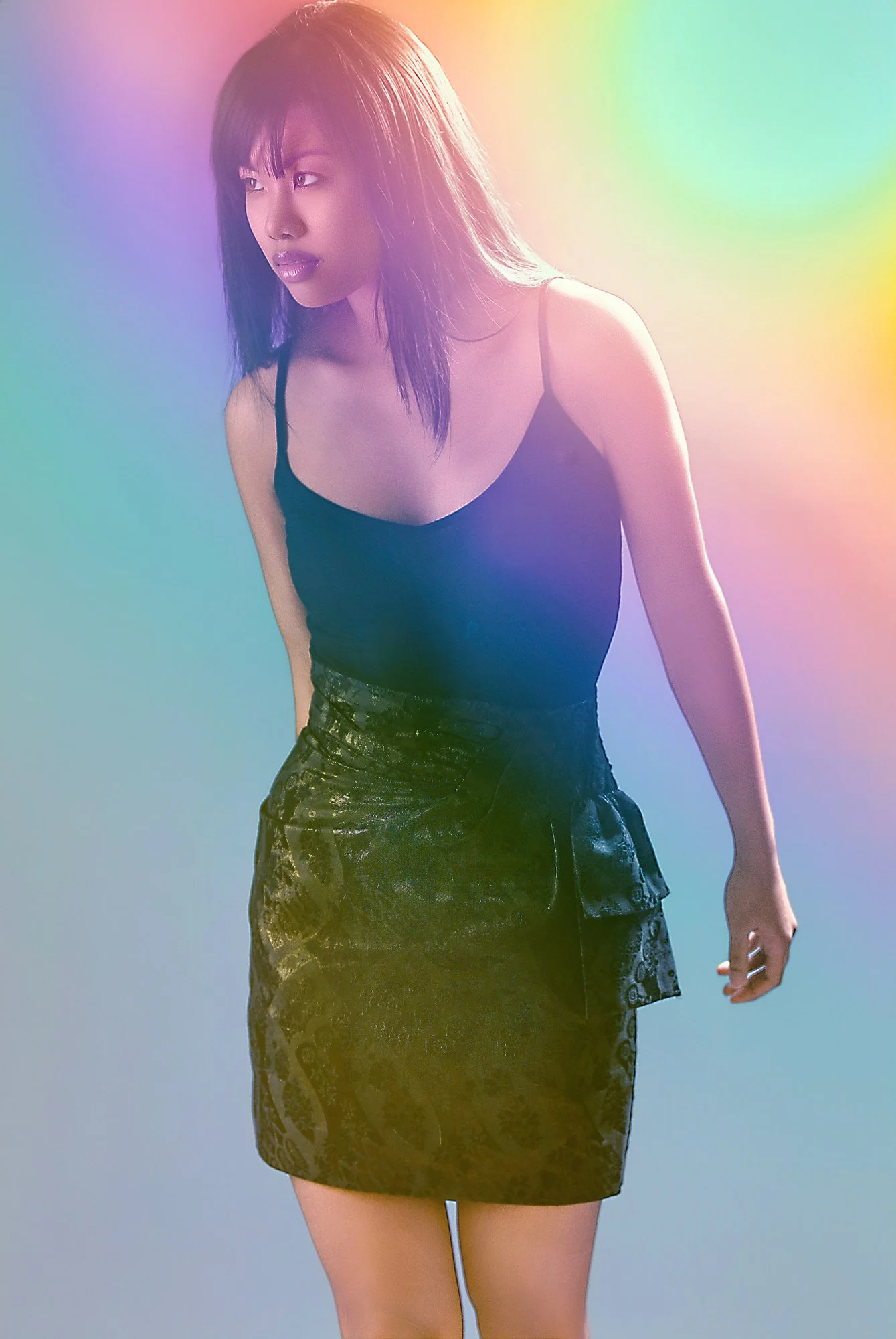 A woman with long dark hair wearing a black spaghetti strap top and a patterned black skirt, standing against a colorful, softly blurred background. Best-Fashion-Portrait-Commercial-Business-Headshots-Corporate- photography-Maryland-Washington D.C.-P