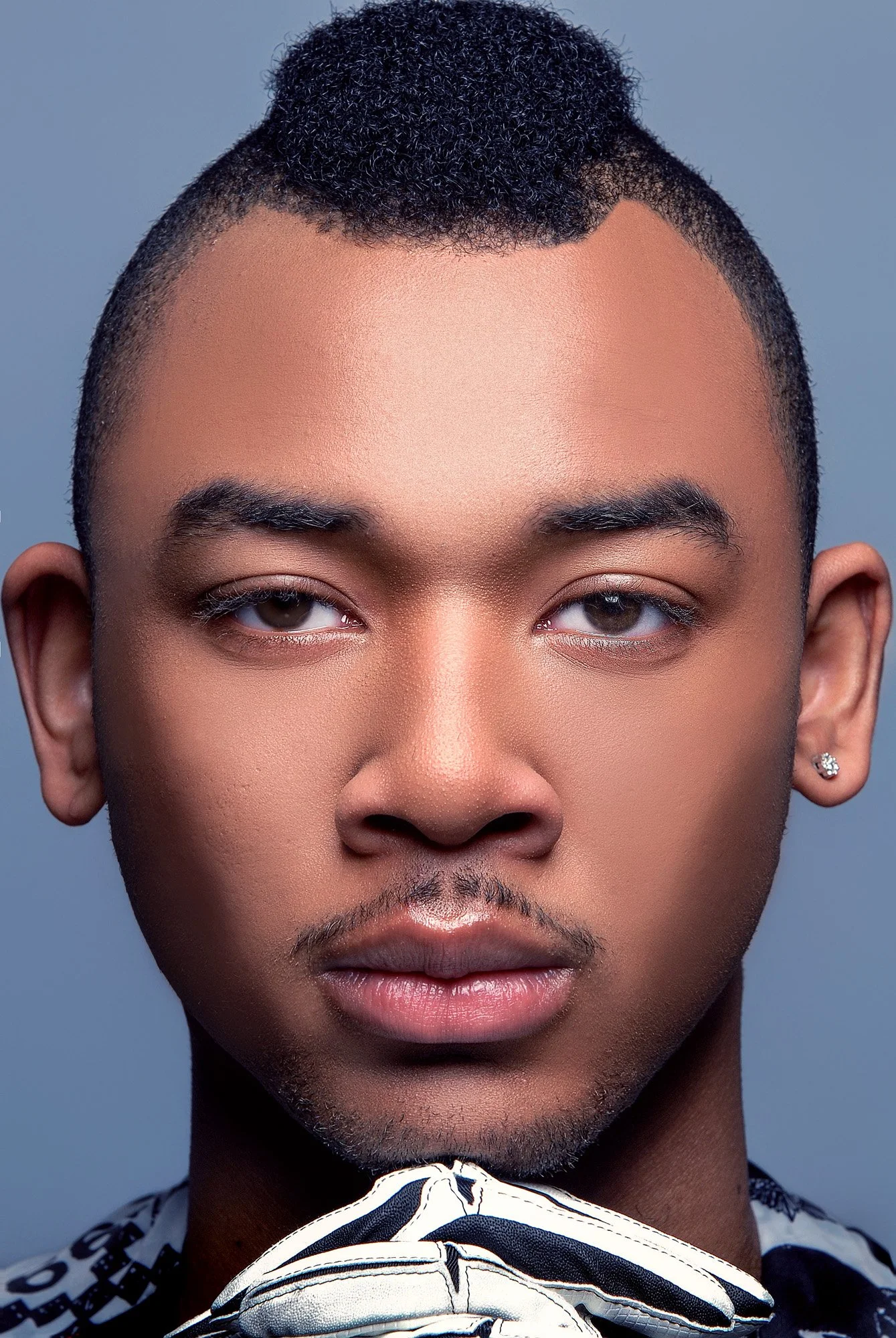 Close-up portrait of a young man with short curly hair, a small mustache and goatee, wearing earrings and a patterned shirt, against a plain background. Best-Fashion-Portrait-Commercial-Business-Headshots-Corporate- photography-Maryland-Washington D.