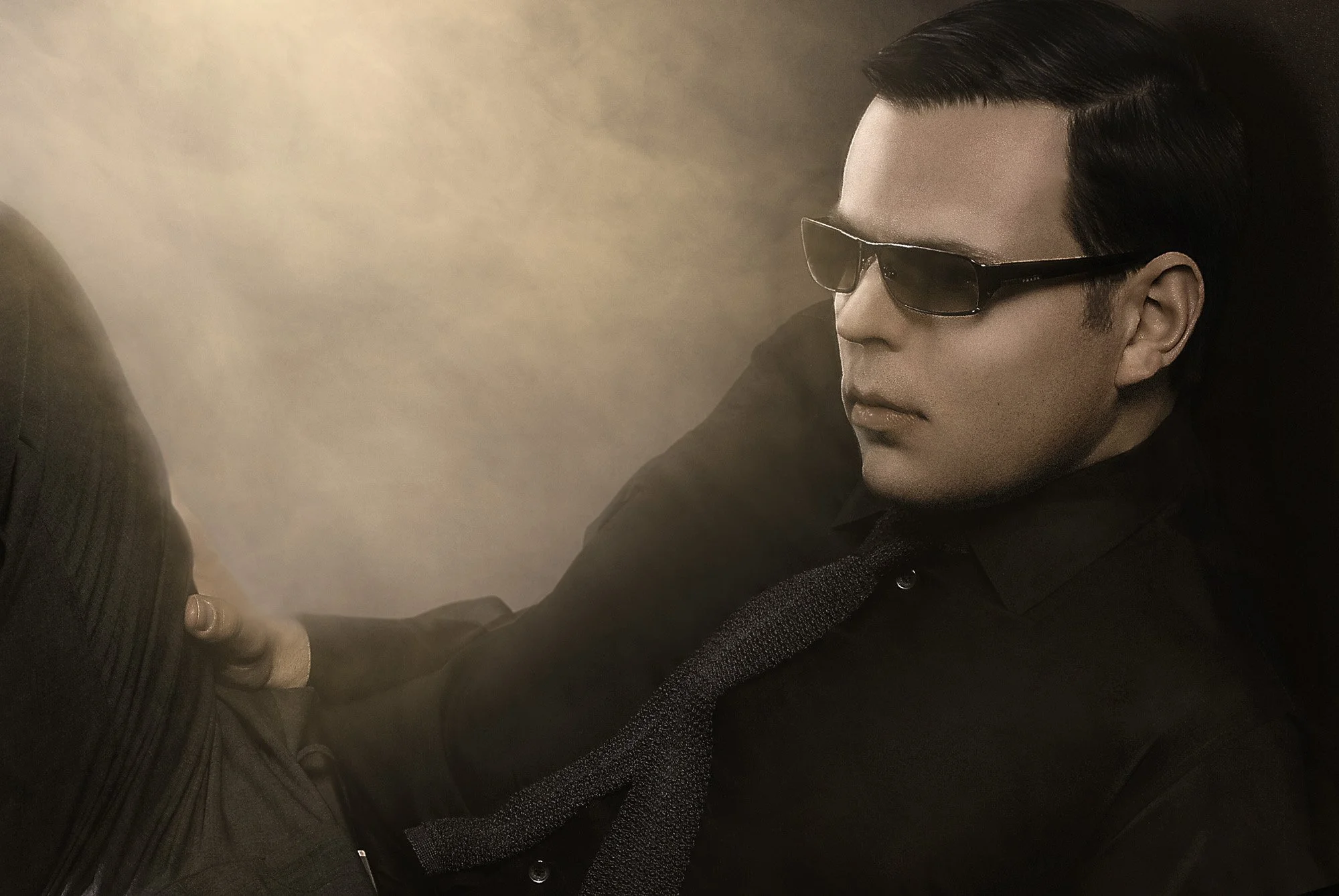 A man with slicked black hair wearing dark sunglasses, a black shirt, and a black tie, sitting against a dark background. Best-Fashion-Portrait-Commercial-Business-Headshots-Corporate- photography-Maryland-Washington D.C.-Pennsylvania-Virginia