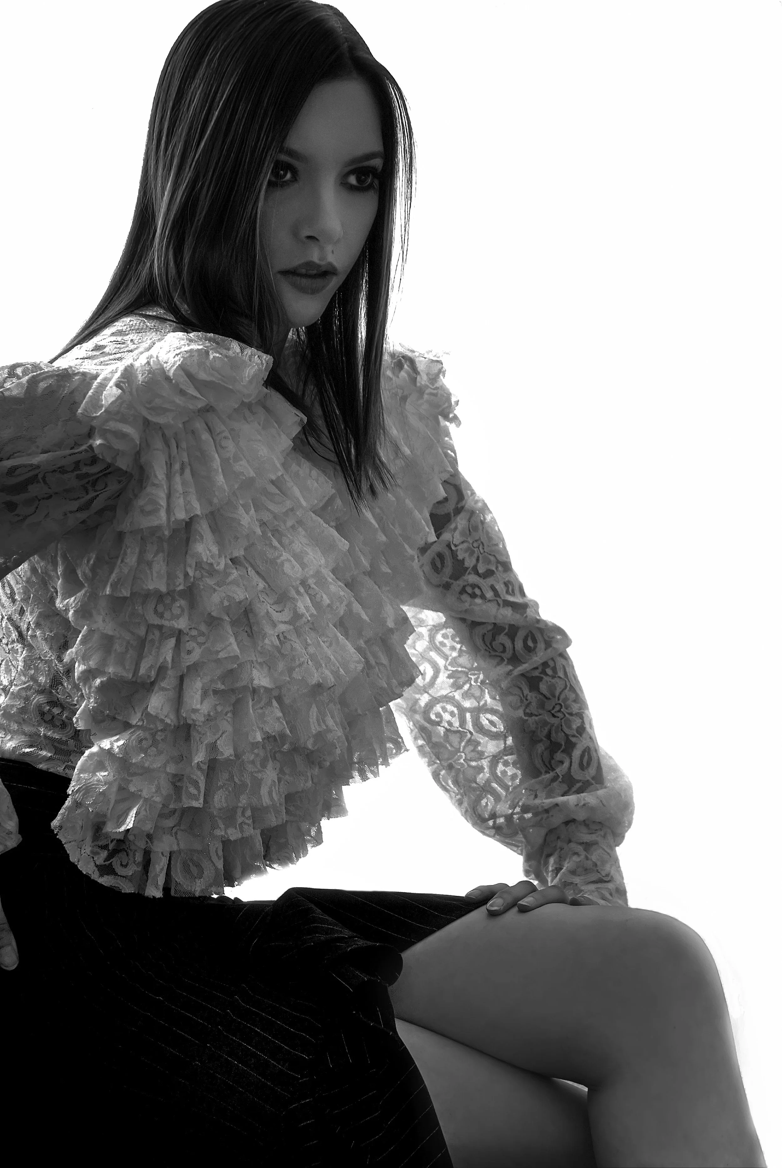 A woman with straight hair wearing a ruffled lace top and a dark skirt, sitting with one knee bent, looking to the side in a black-and-white photo. Best-Fashion-Portrait-Commercial-Business-Headshots-Corporate- photography-Maryland-Washington D.C.-Pe