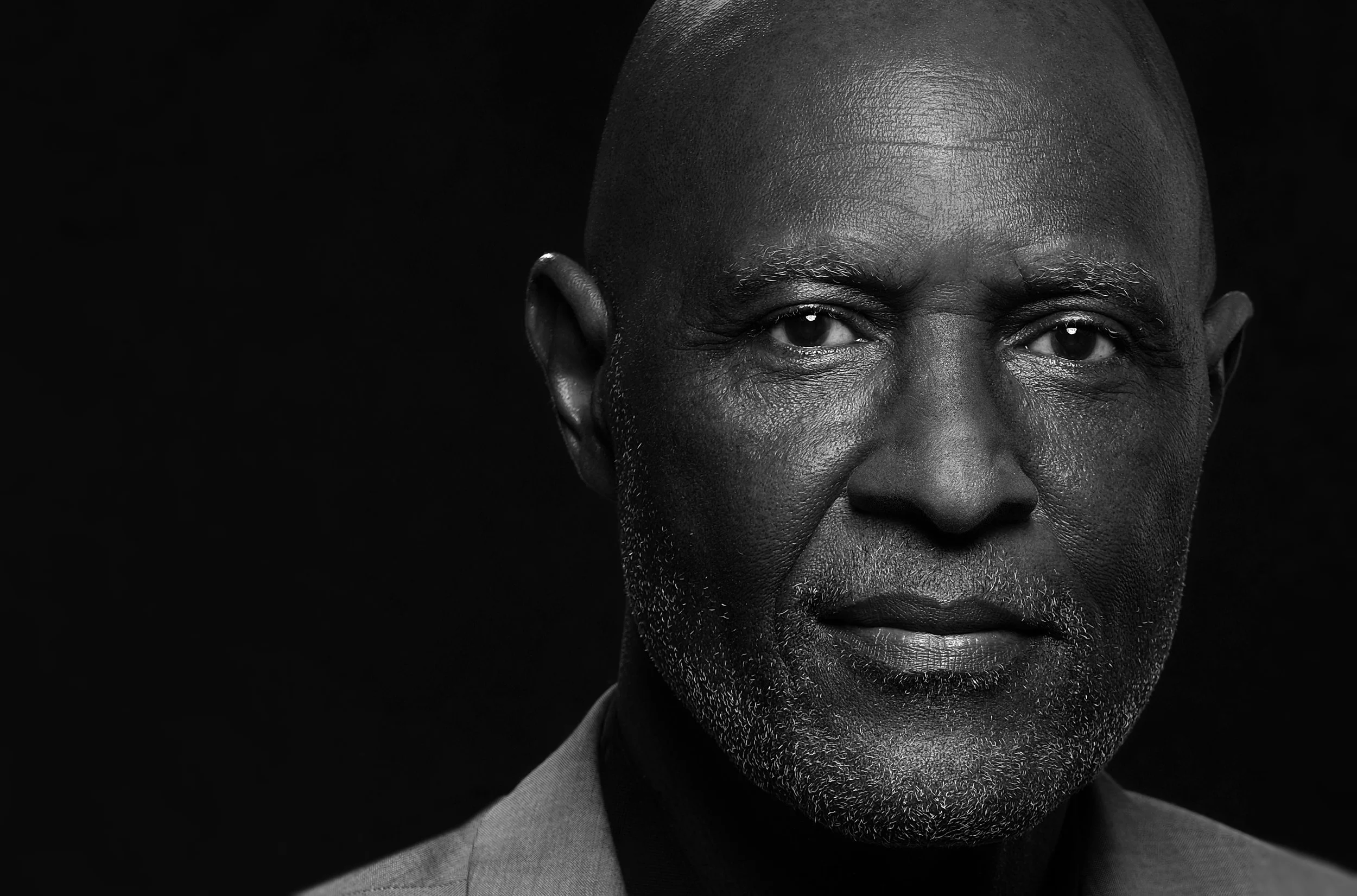Black and white close-up portrait of a middle-aged man with a shaved head, sporting a beard, dressed in a suit, against a dark background. Best-Fashion-Portrait-Commercial-Business-Headshots-Corporate- photography-Maryland-Washington D.C.-Pennsylvani
