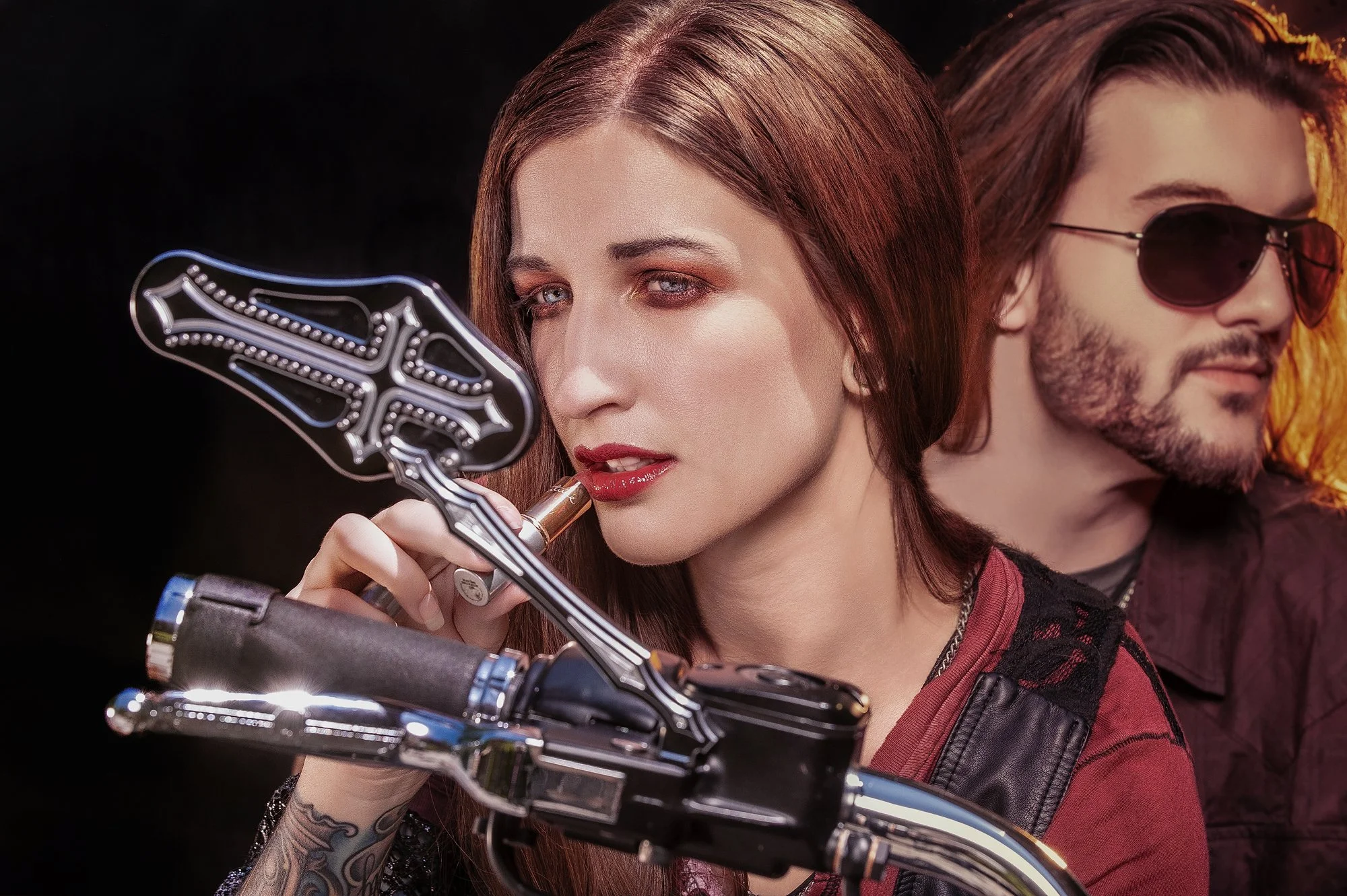 A woman with red hair and makeup holding a motorcycle handlebar lever, with a man with long hair and sunglasses in the background. Best-Fashion-Portrait-Commercial-Business-Headshots-Corporate- photography-Maryland-Washington D.C.-Pennsylvania-Virgin