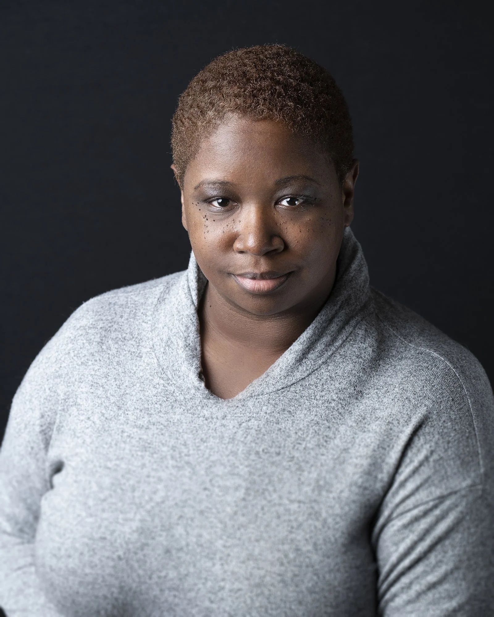 Portrait of a person wearing a gray sweater against a dark background.