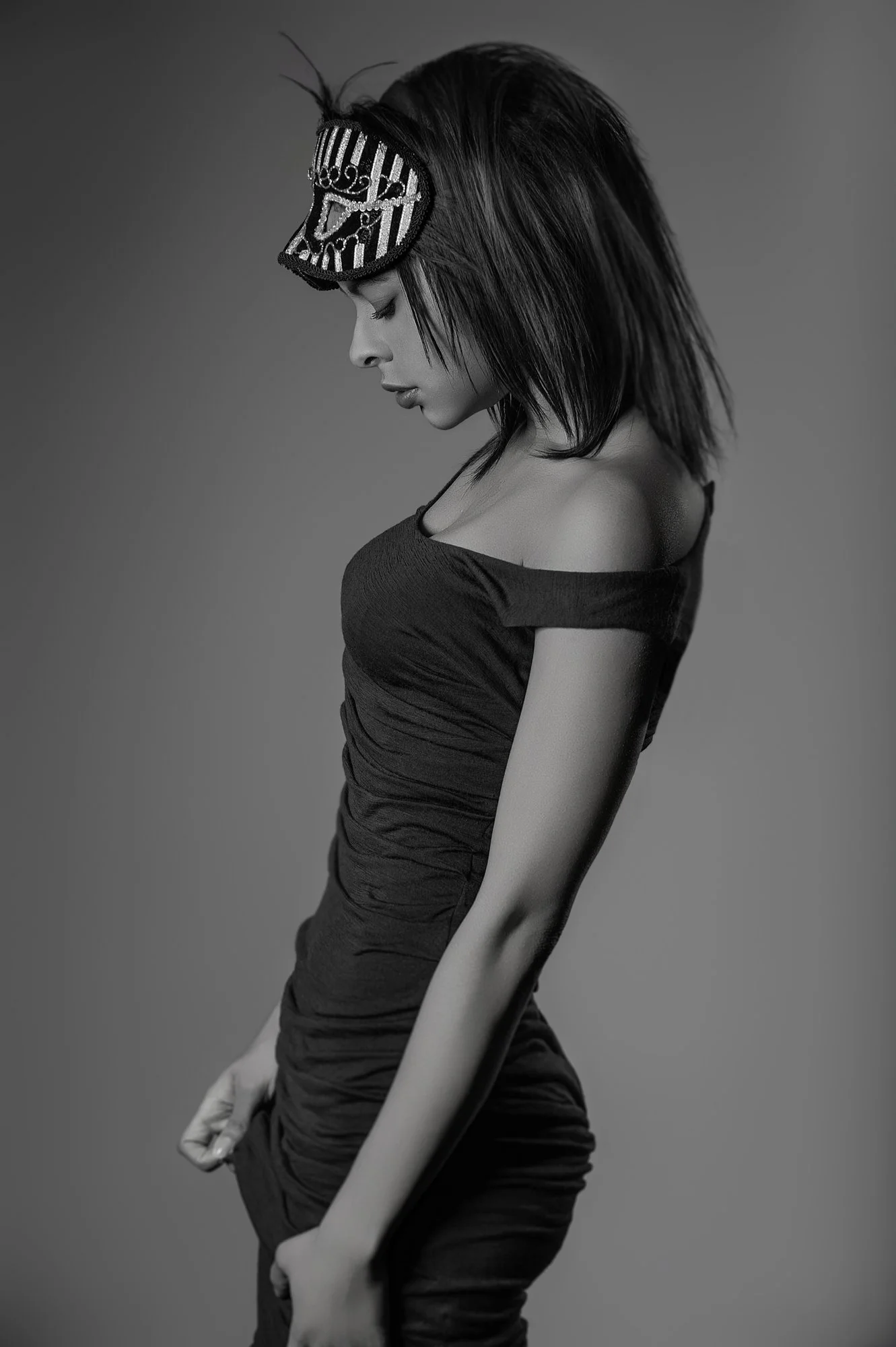 Black and white photo of a woman with shoulder-length hair wearing a dark, off-the-shoulder dress and a decorative mask on her forehead, posing with her head bowed and eyes closed. Best-Fashion-Portrait-Commercial-Business-Headshots-Corporate- photog