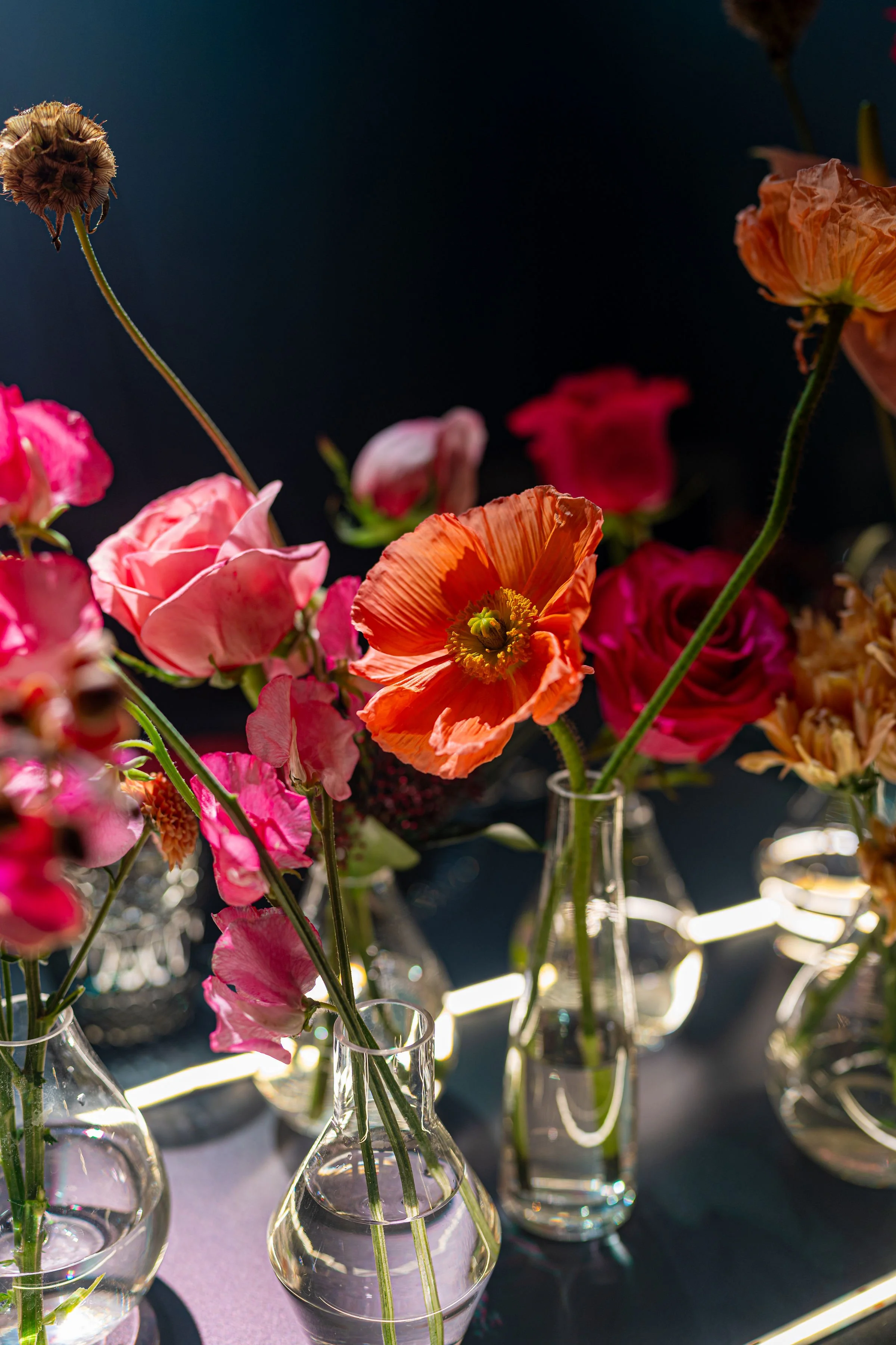 Vase with colorful flowers including pink, red, and orange blooms against a dark background.