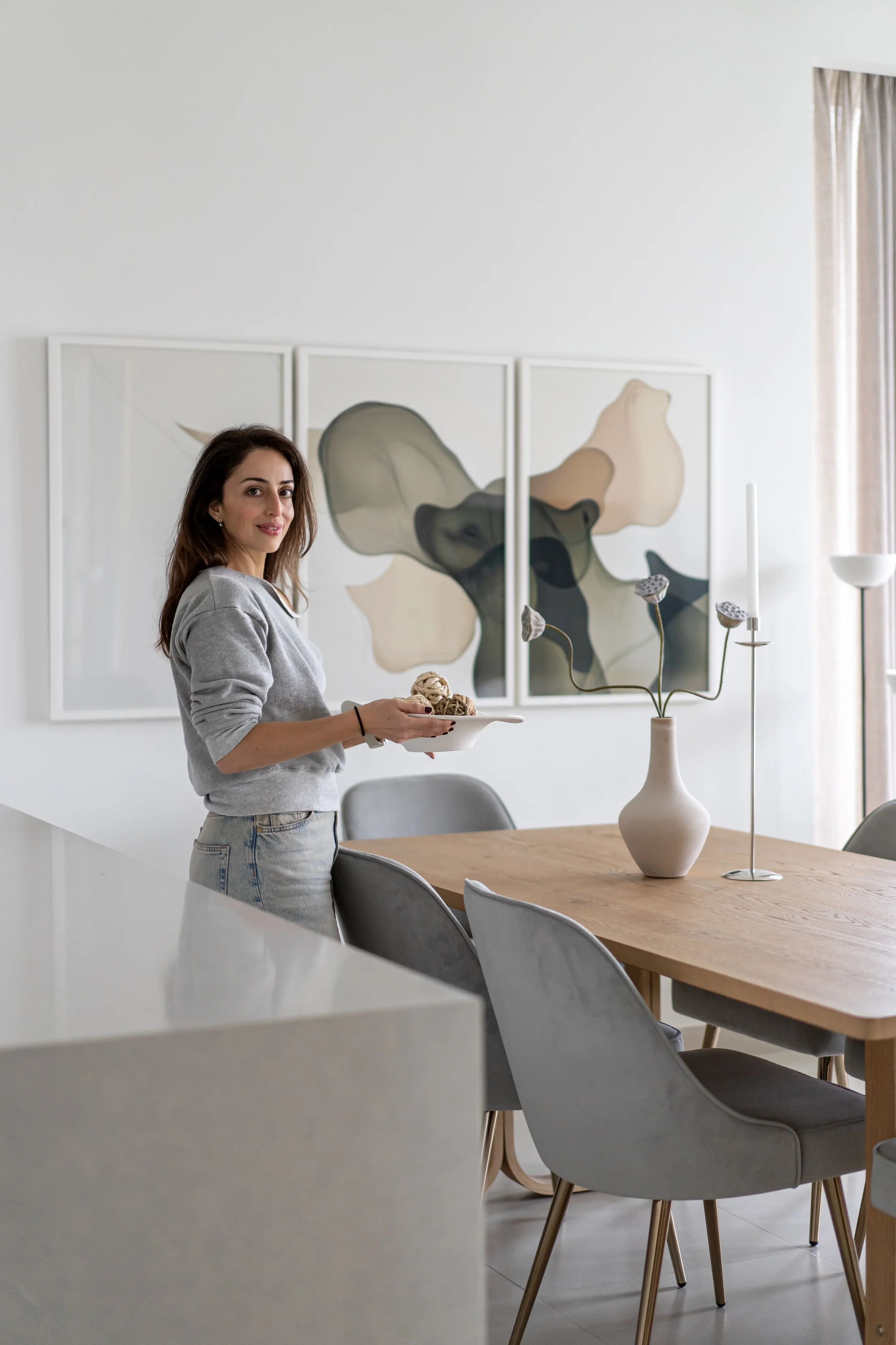 Woman holding a plate of ice cream in a modern dining room with abstract artwork on the wall and a minimalist vase on the table.