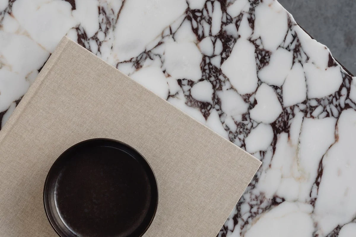 Empty black ceramic bowl on a beige cloth napkin placed on a white marble table with dark brown veining.