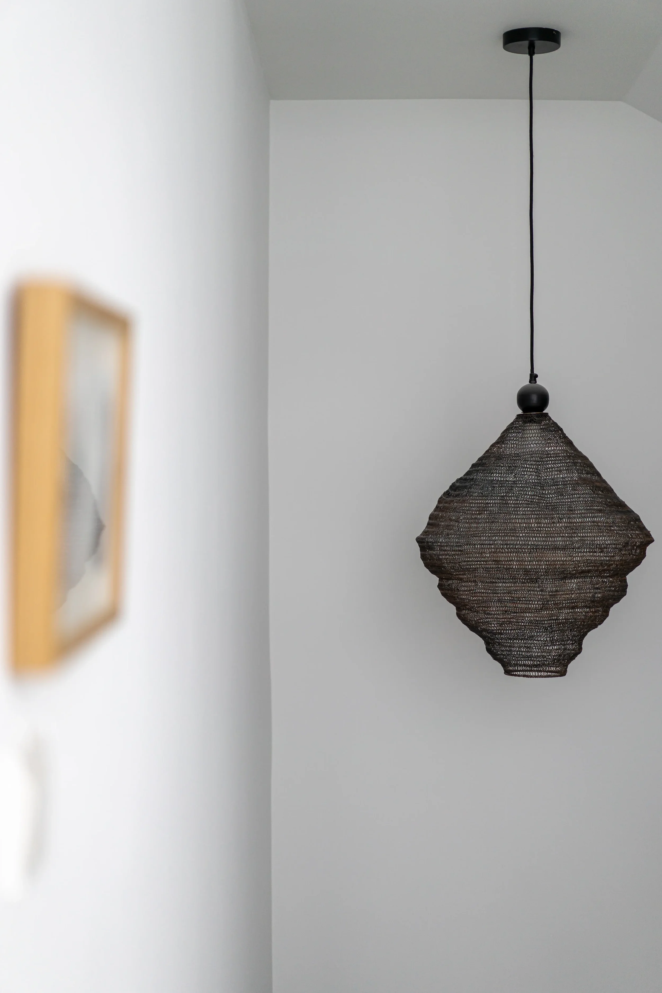 A modern black pendant light fixture hanging from the ceiling in a room with white walls.