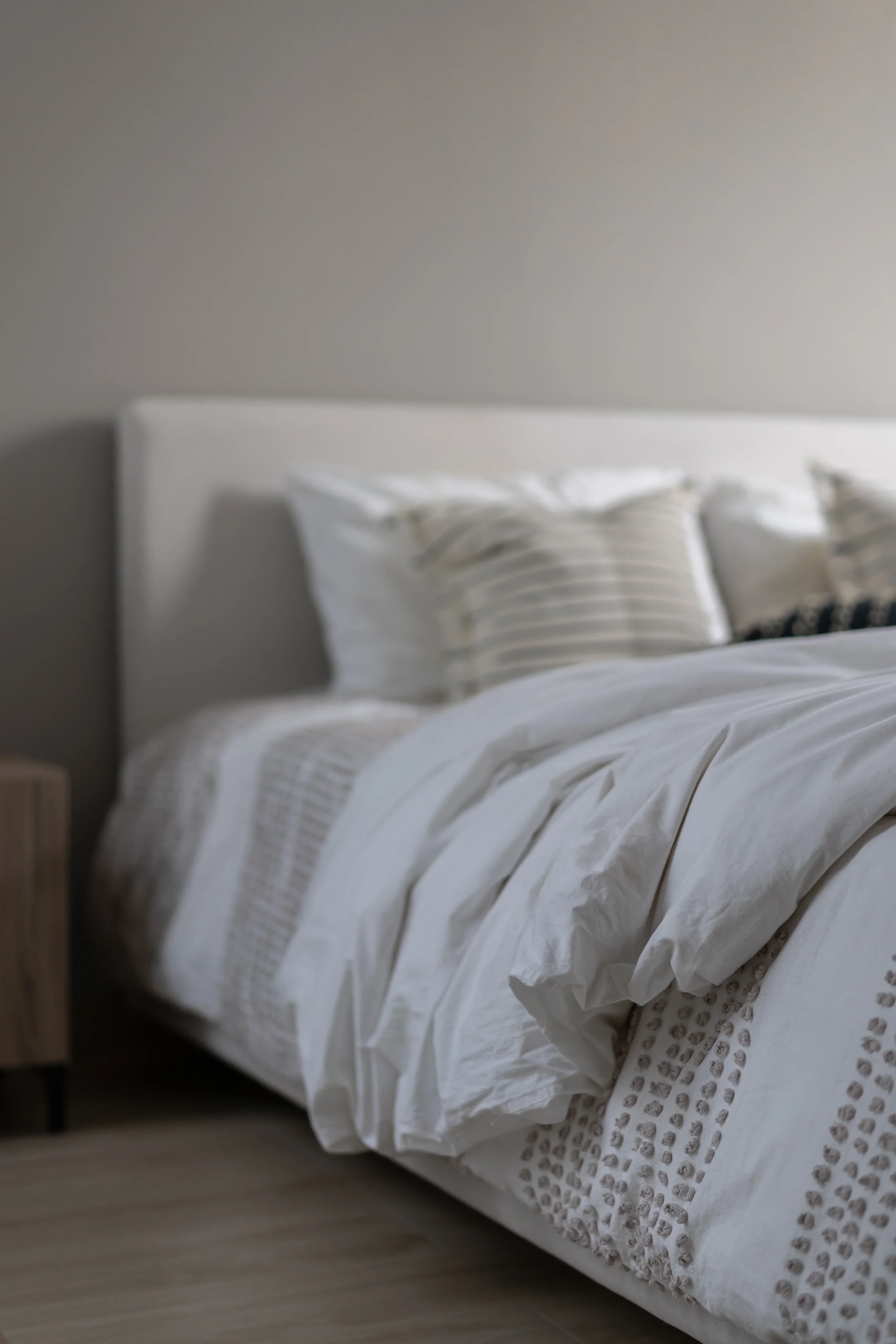 Unmade bed with white bedding and pillows in a bedroom, beige wall in the background.