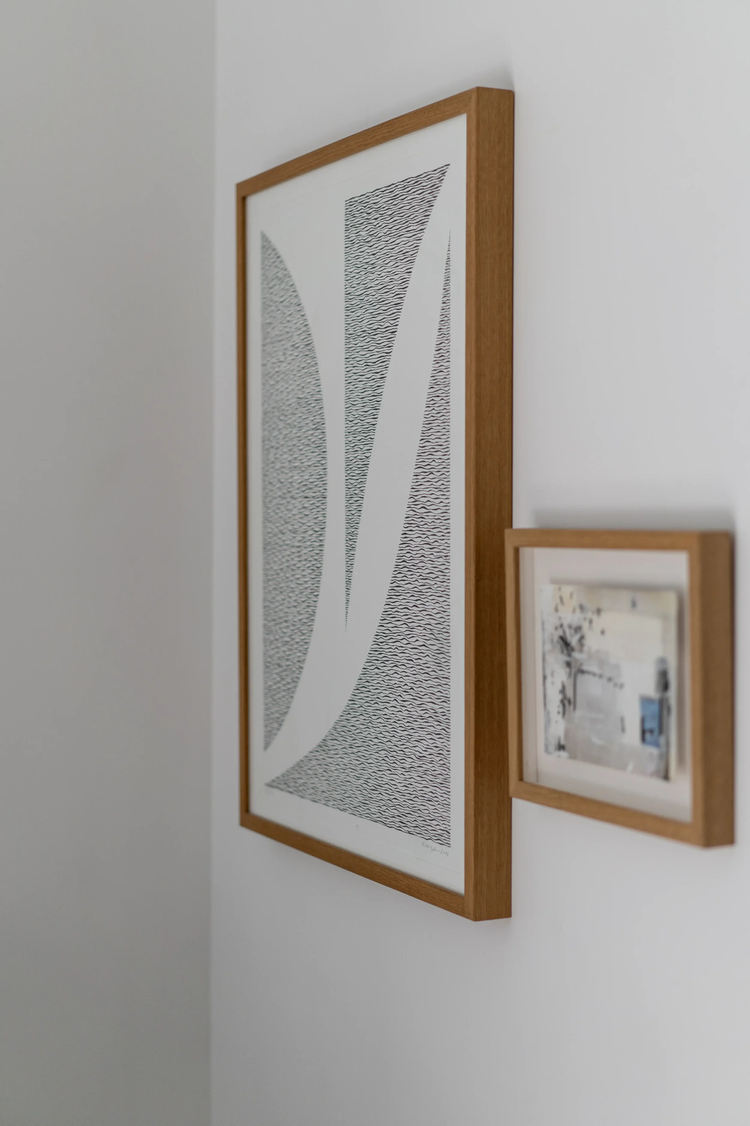 Close-up of two framed pictures hanging on a white wall, with the larger piece featuring abstract black lines and shapes.