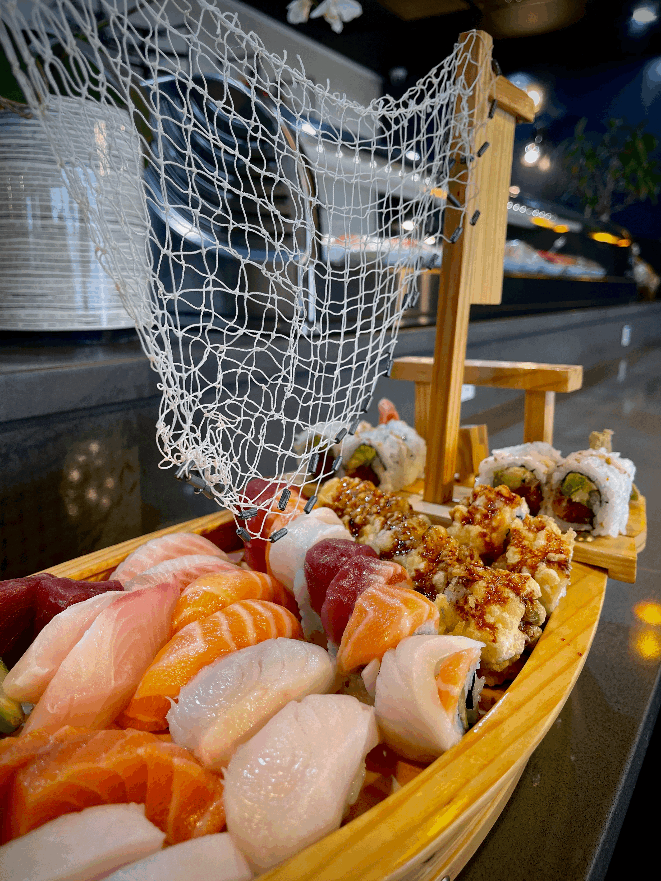 Sushi platter with various types of nigiri and sushi rolls displayed on a wooden boat-shaped tray at a restaurant.