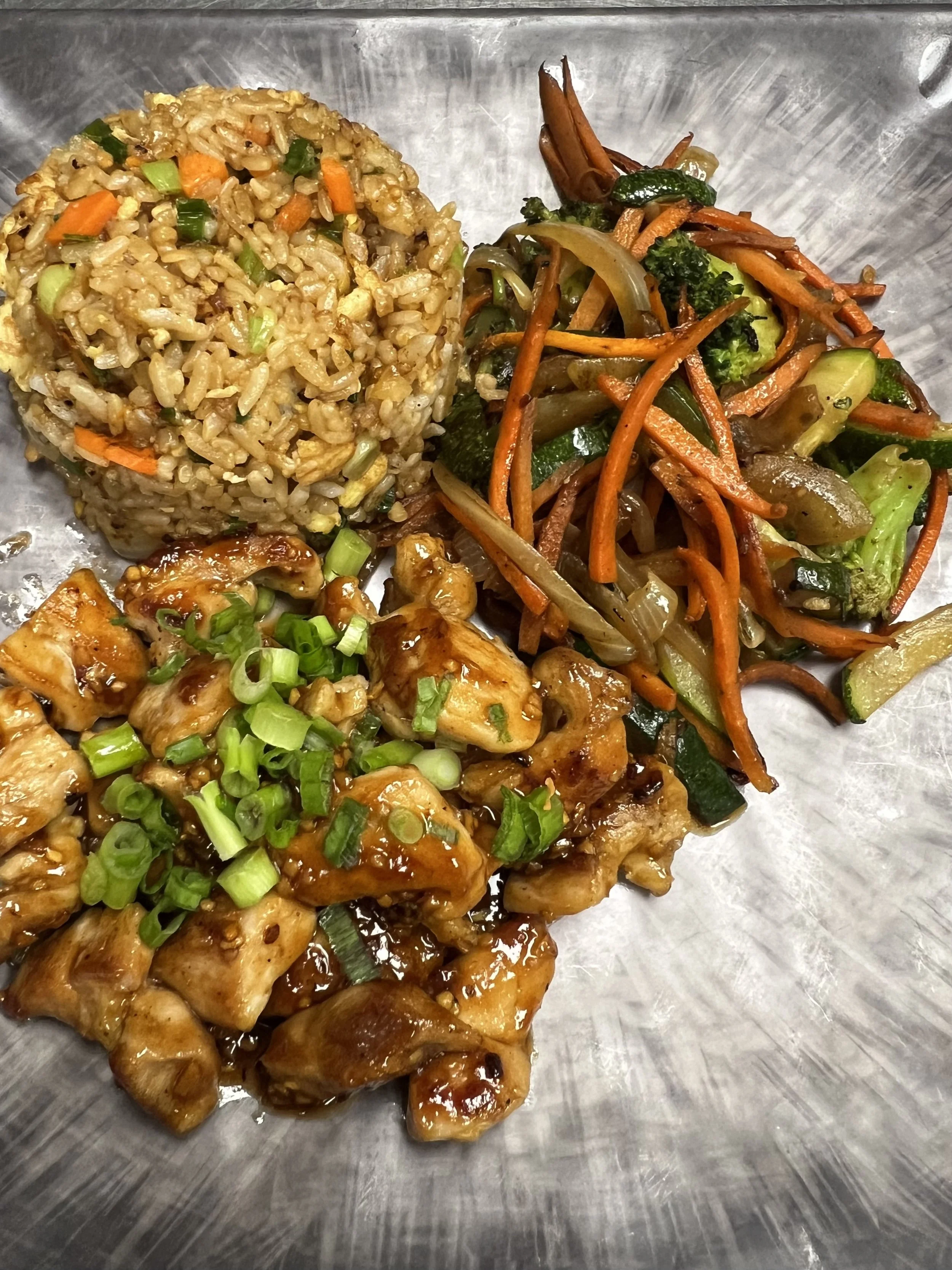 Plate of Asian stir-fried vegetables with broccoli, carrots, and onions, alongside fried rice and chicken with green onions in a sauce.