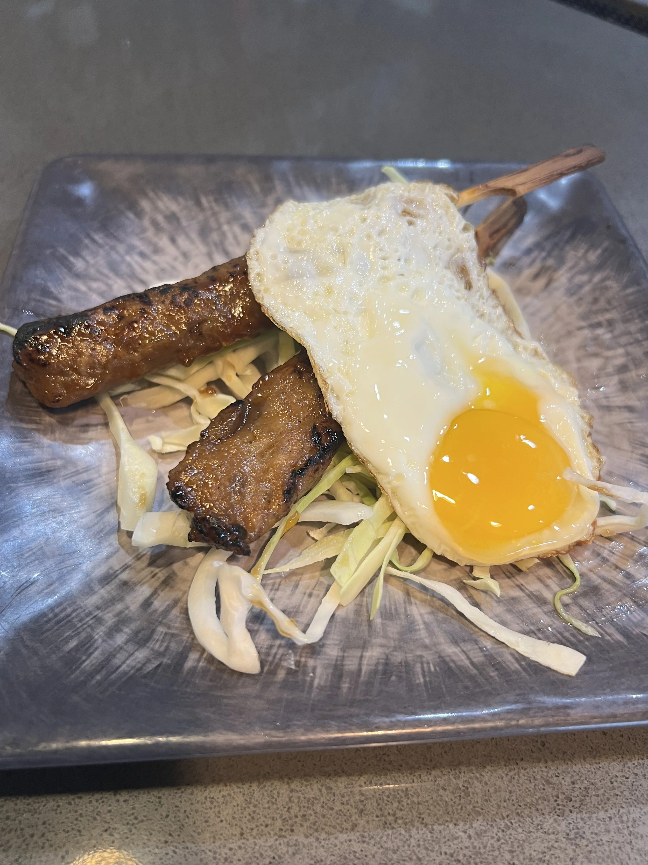Skewered grilled chicken meatball, a fried egg with a runny yolk, and shredded cabbage.