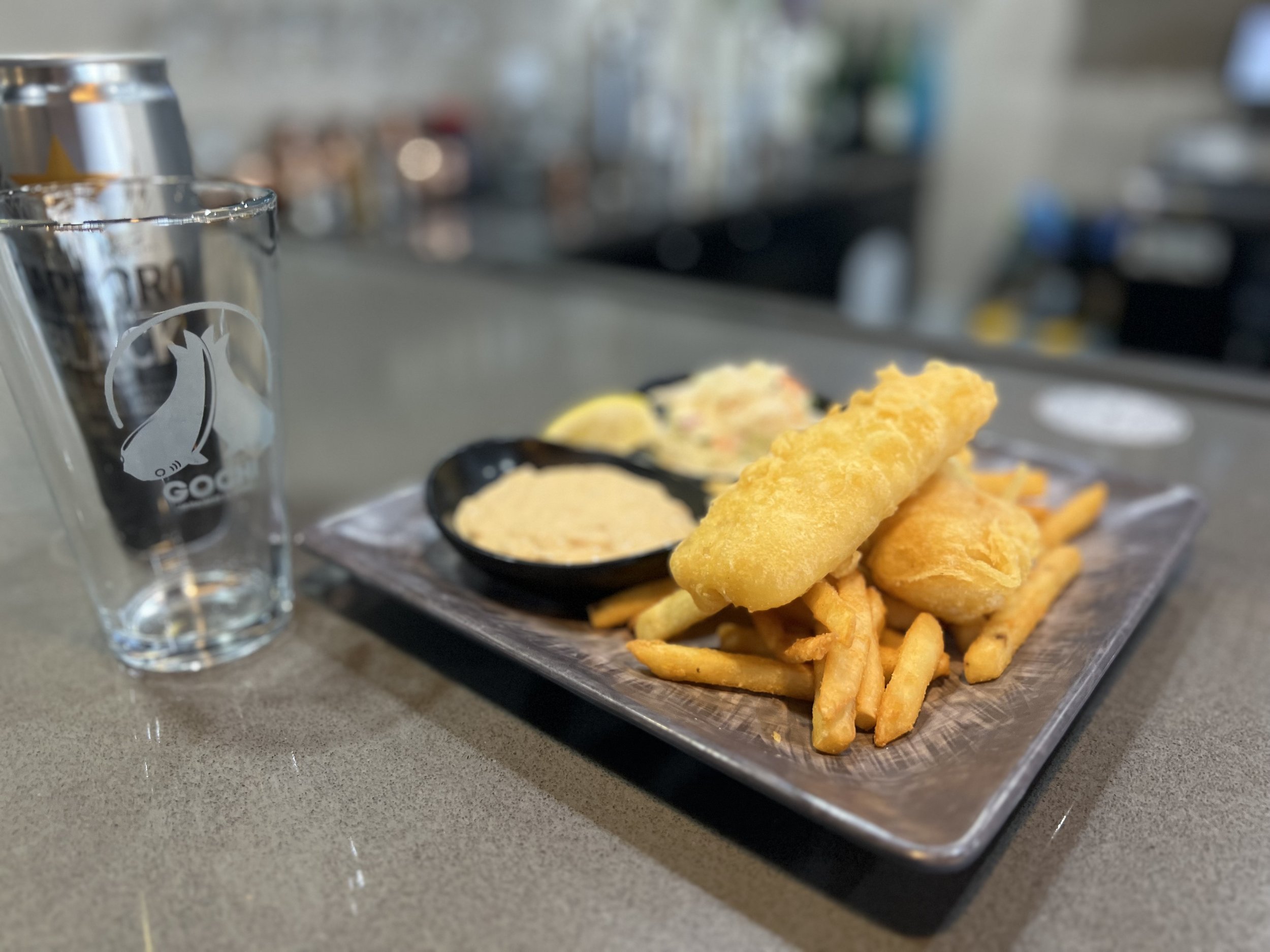 A tray of fried fish and chips with tartar sauce, lemon wedge, and a glass of water on a counter in a restaurant.