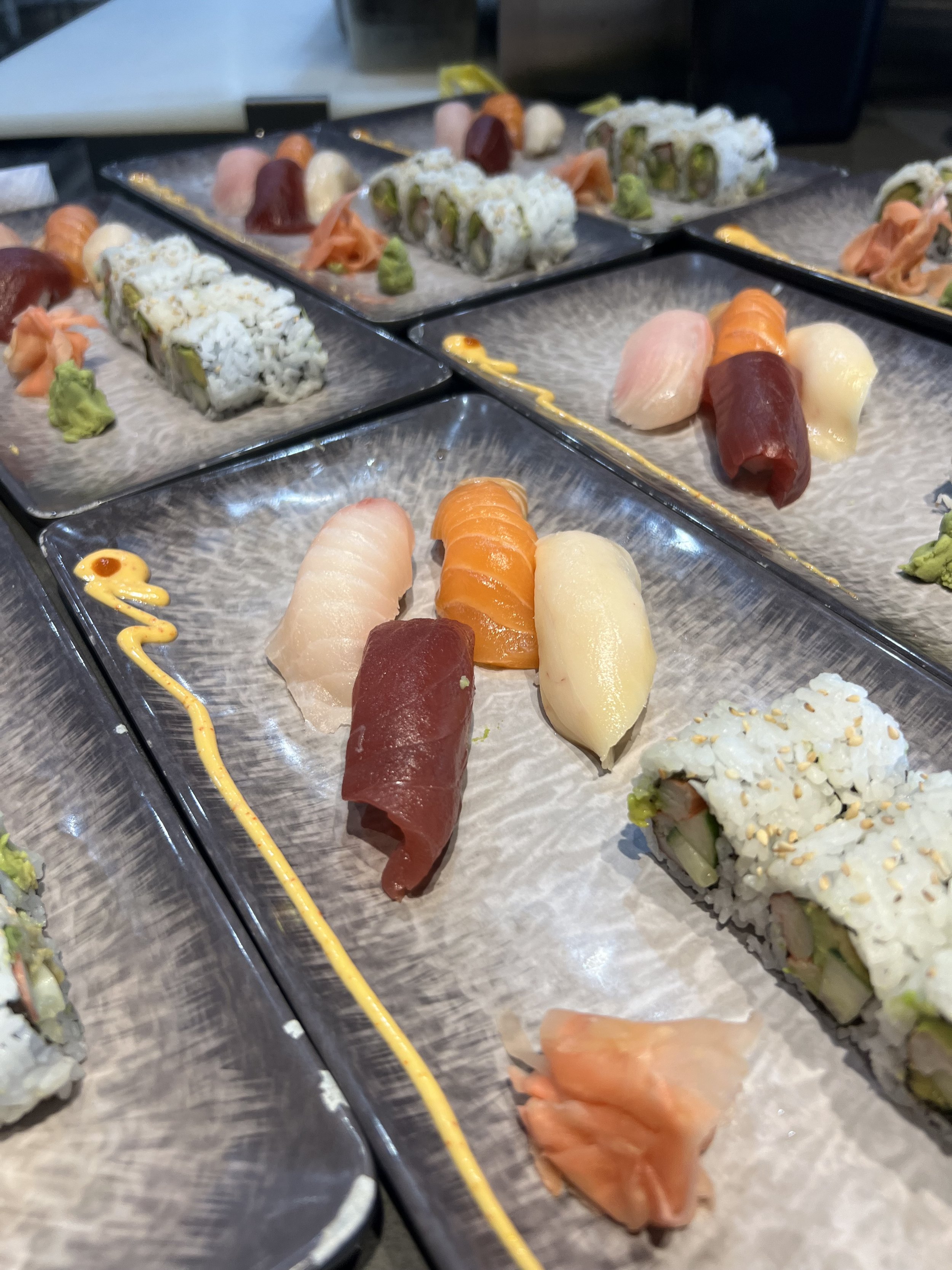 Sushi lunch special combo serve with soup or salad. Assortment of sushi dishes including salmon, tuna, and white fish sashimi, crab roll, and various sushi rolls with wasabi, pickled ginger, and sauces.