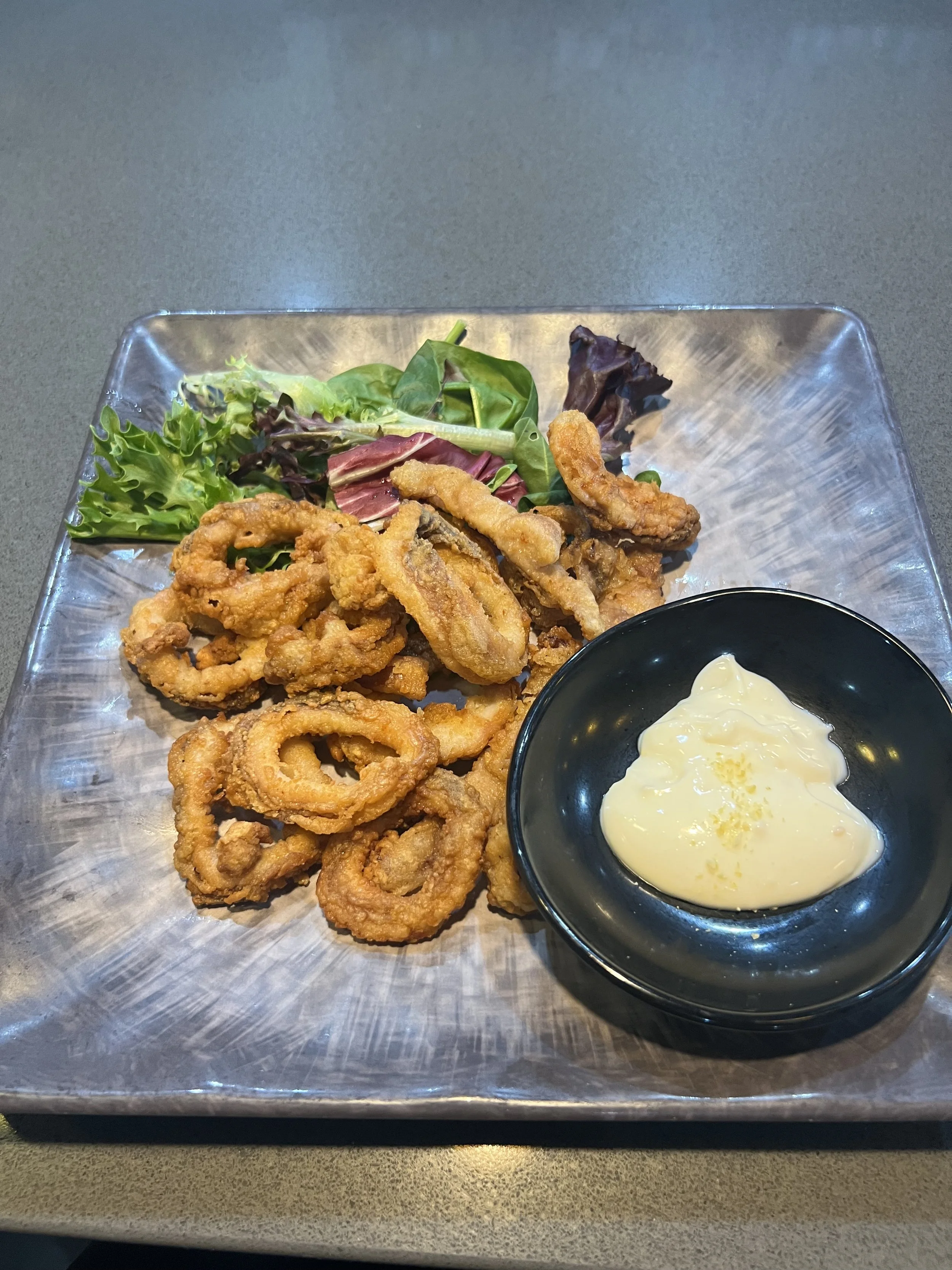 Plate of fried calamari rings, mixed greens salad, and a small bowl of creamy yuzu mayo