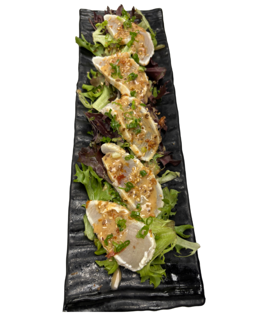 A black rectangular plate holding five pieces of sashimi served on a bed of mixed greens, garnished with chopped green onions and a drizzle of sauce.