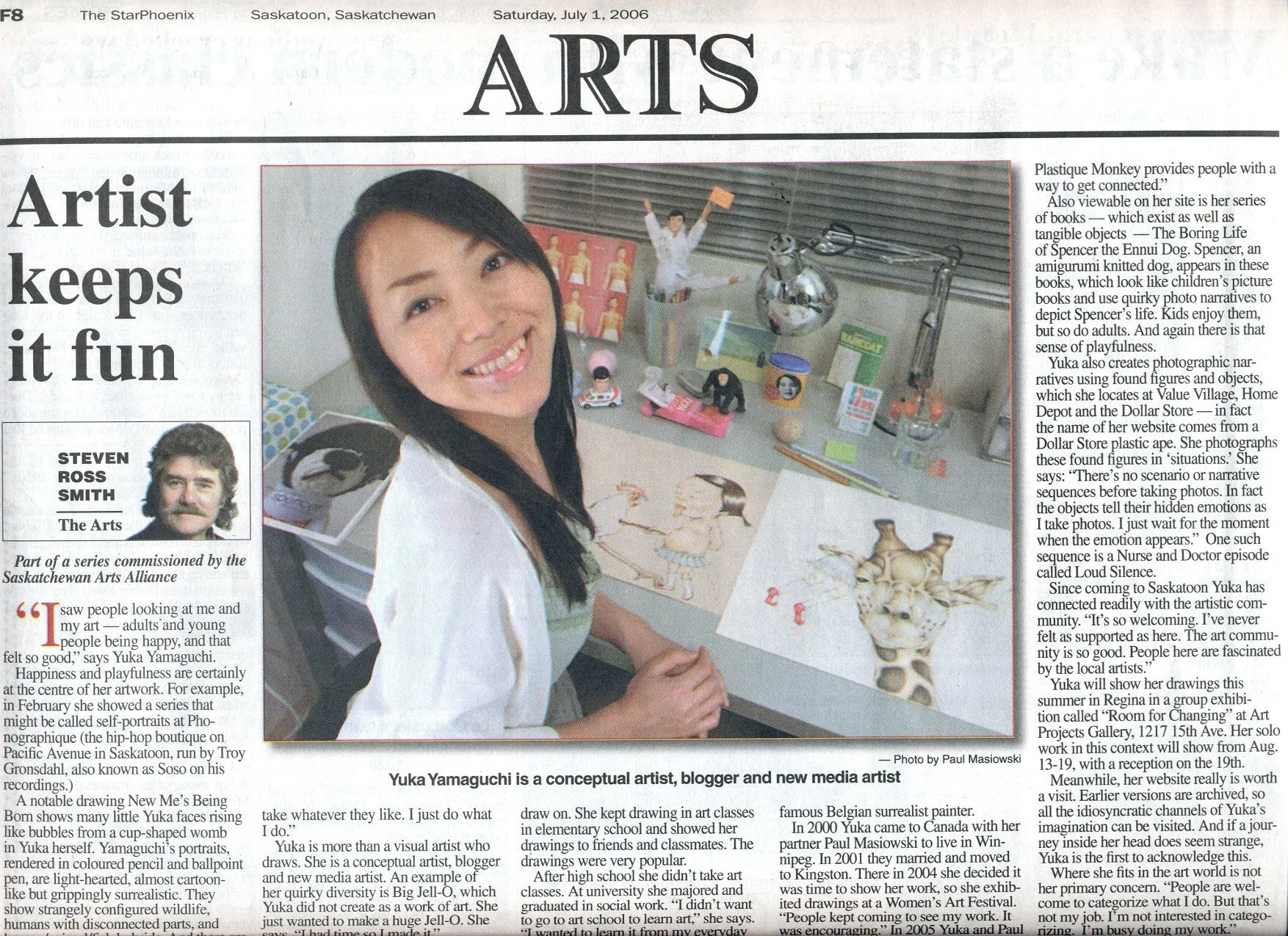 Newspaper article featuring an artist named Yuka Yamaguchi. The image shows Yuka smiling in front of her art workspace with drawings and various art materials on the desk. The headline reads "Artist keeps it fun," and the article discusses Yuka's wor