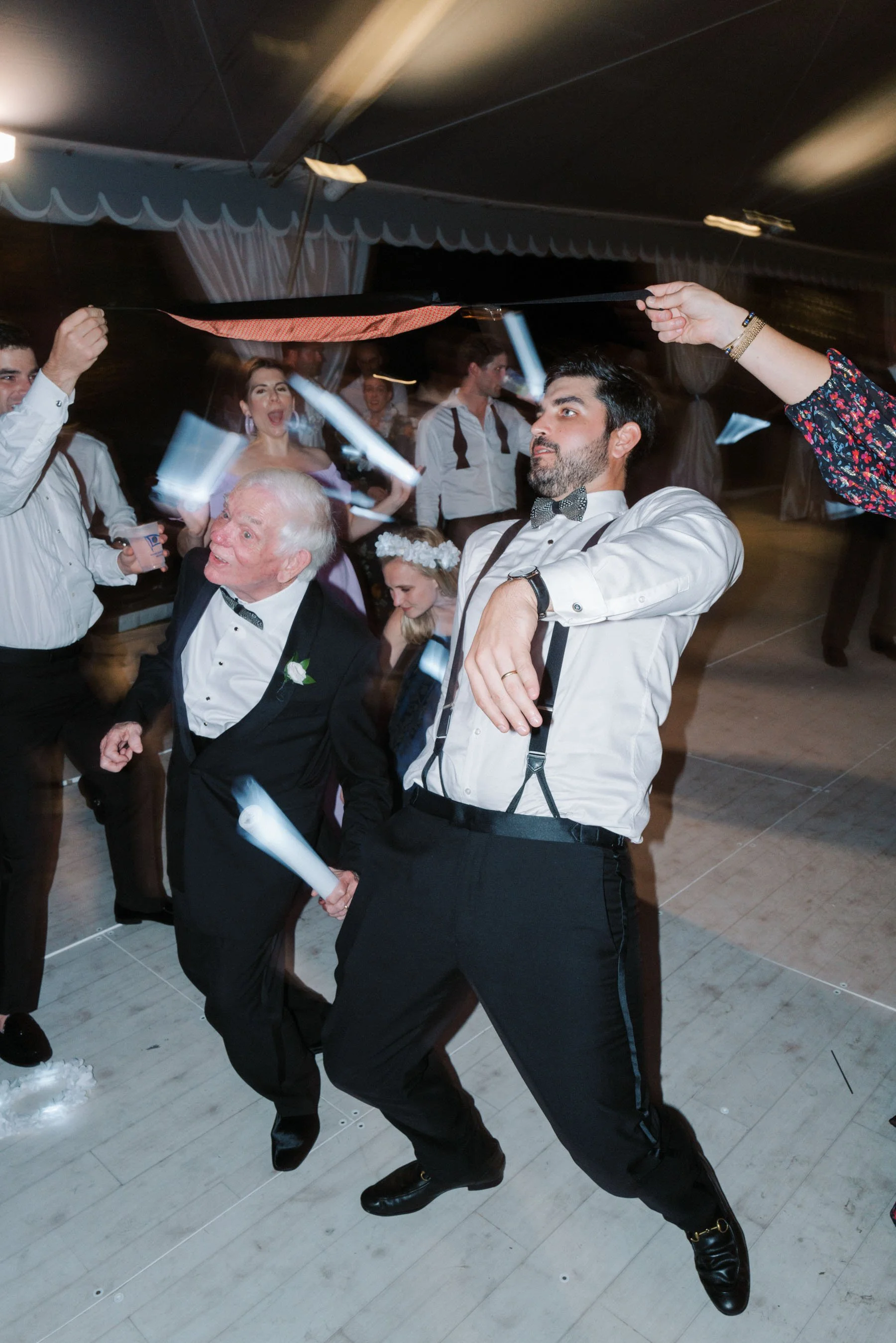 People dancing and celebrating at a wedding reception, holding glow sticks, with a joyful atmosphere.