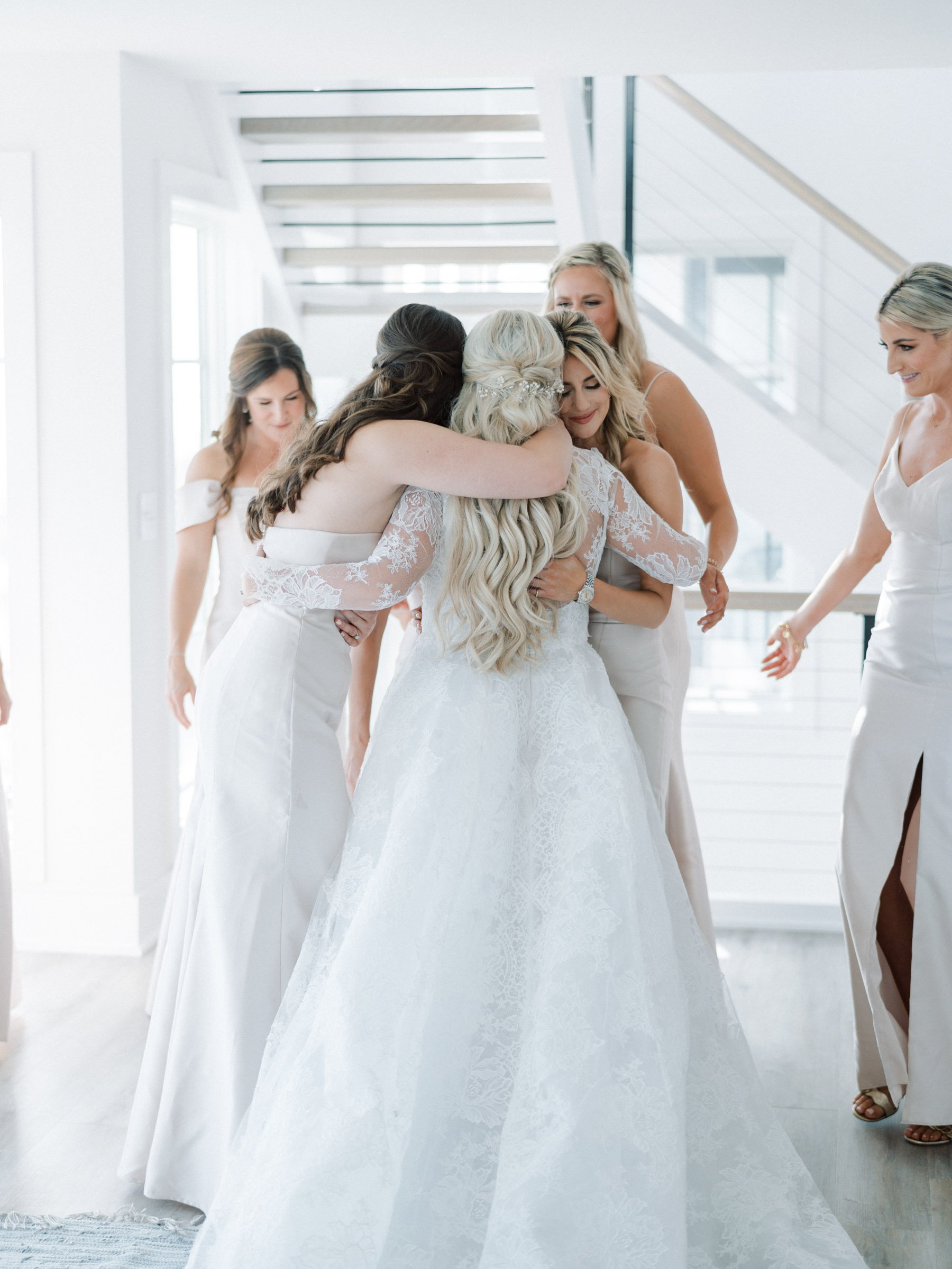 Bridal party hugging and celebrating in a bright, modern home with white walls and staircase.