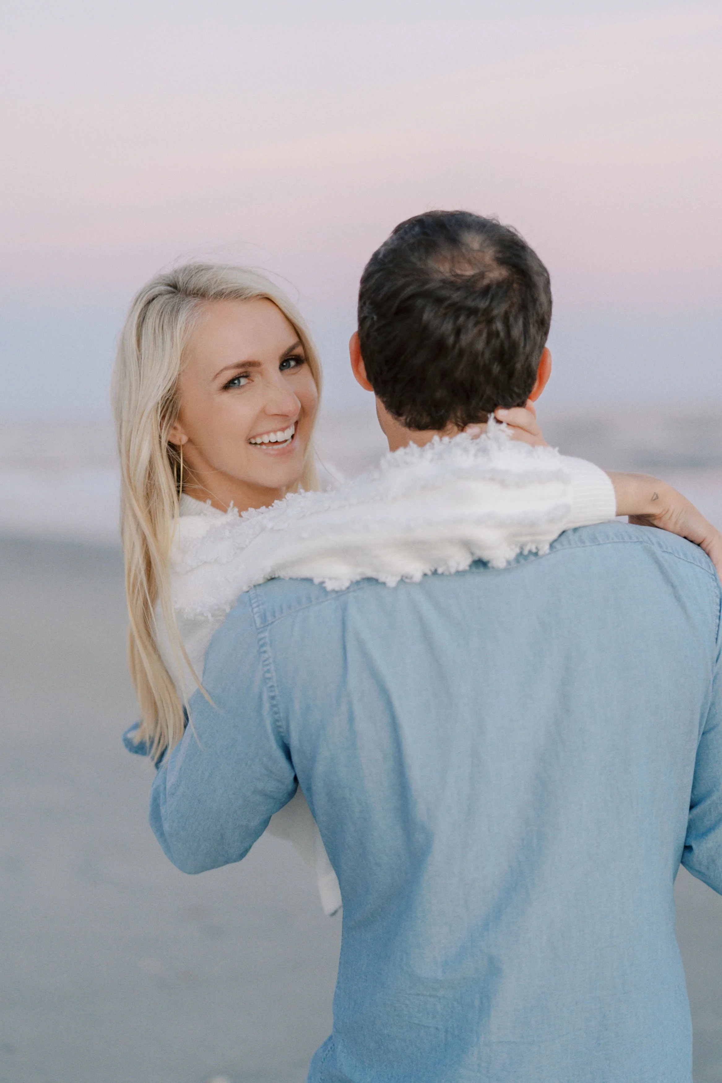 A woman with blonde hair smiling at a man holding her at the beach during sunset at Isle of Palms beach.