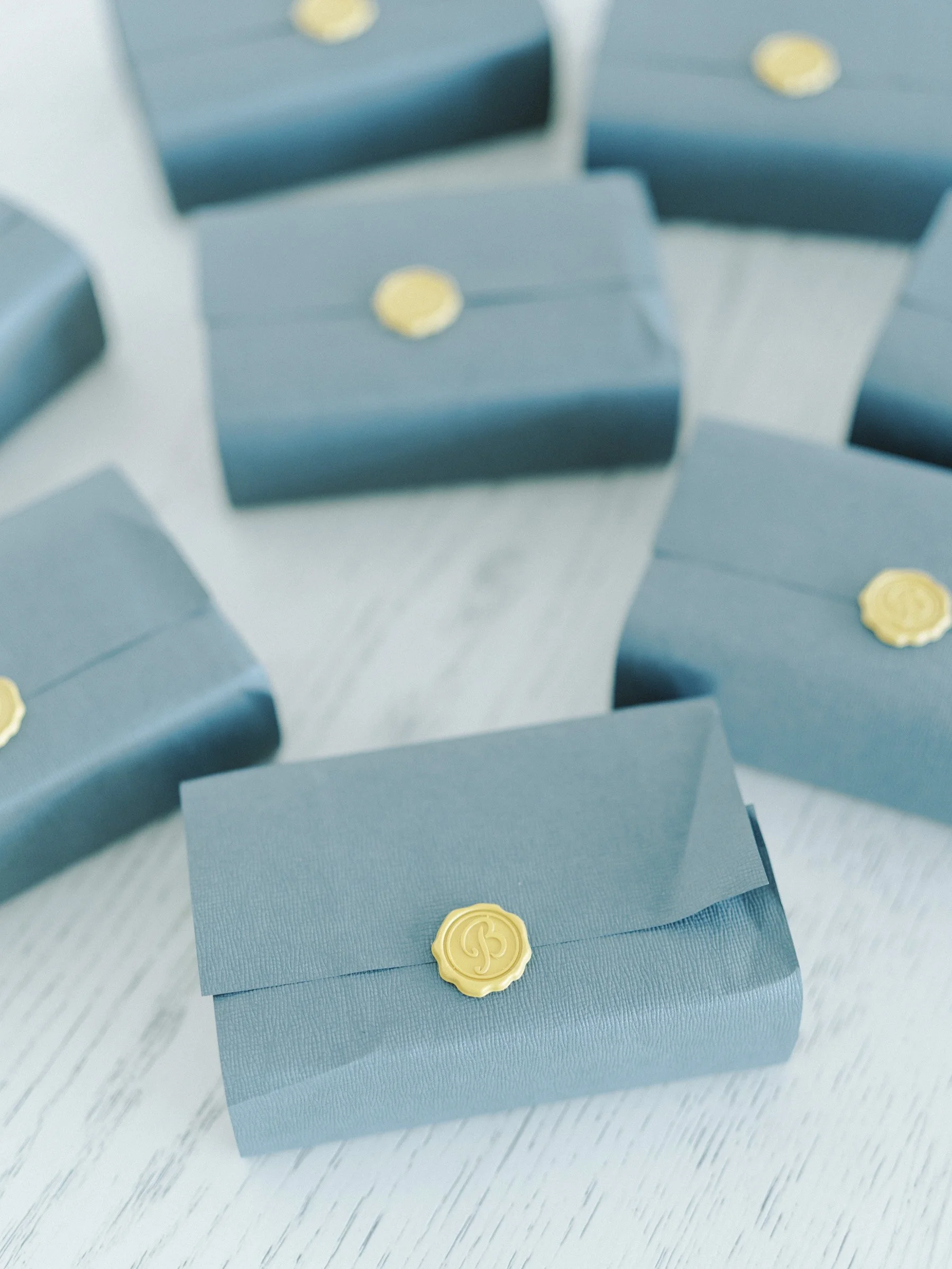 Multiple blue gift boxes with beige wax seals on a light-colored surface.