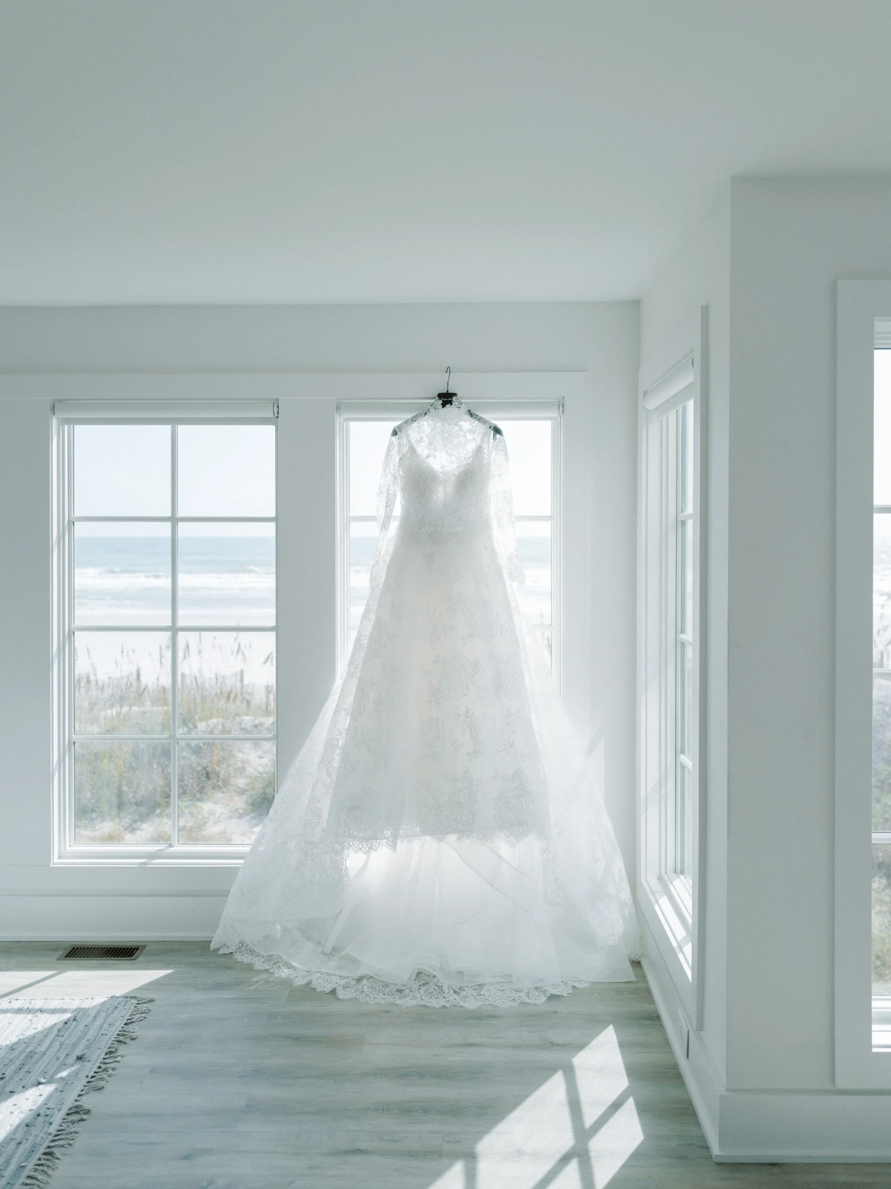A white wedding dress hanging on a hanger in front of a window with ocean view, sunlight shining through at Figure 8 Island Yacht Club. 