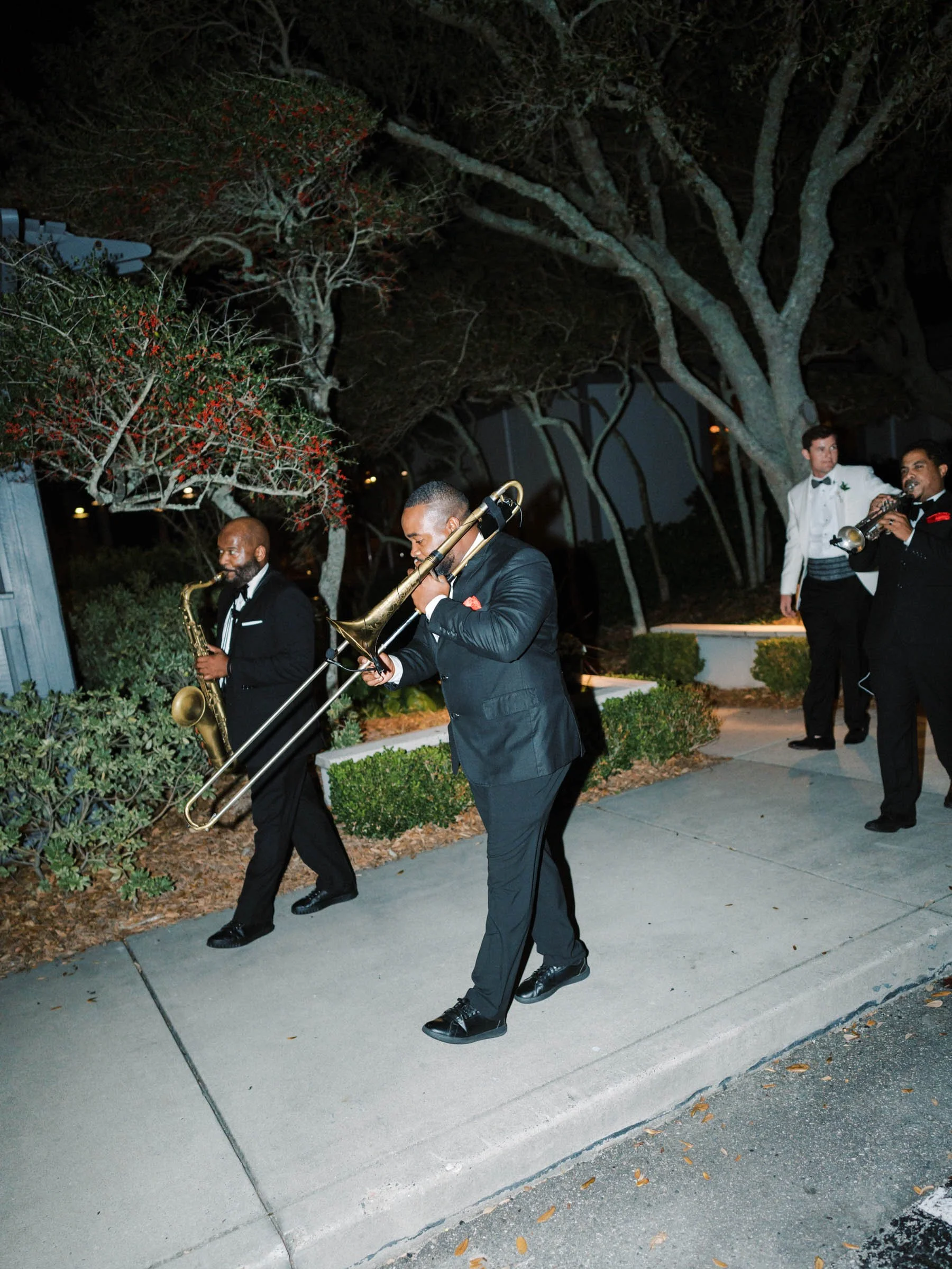Jazz band playing outdoors at night with trees and bushes in the background.