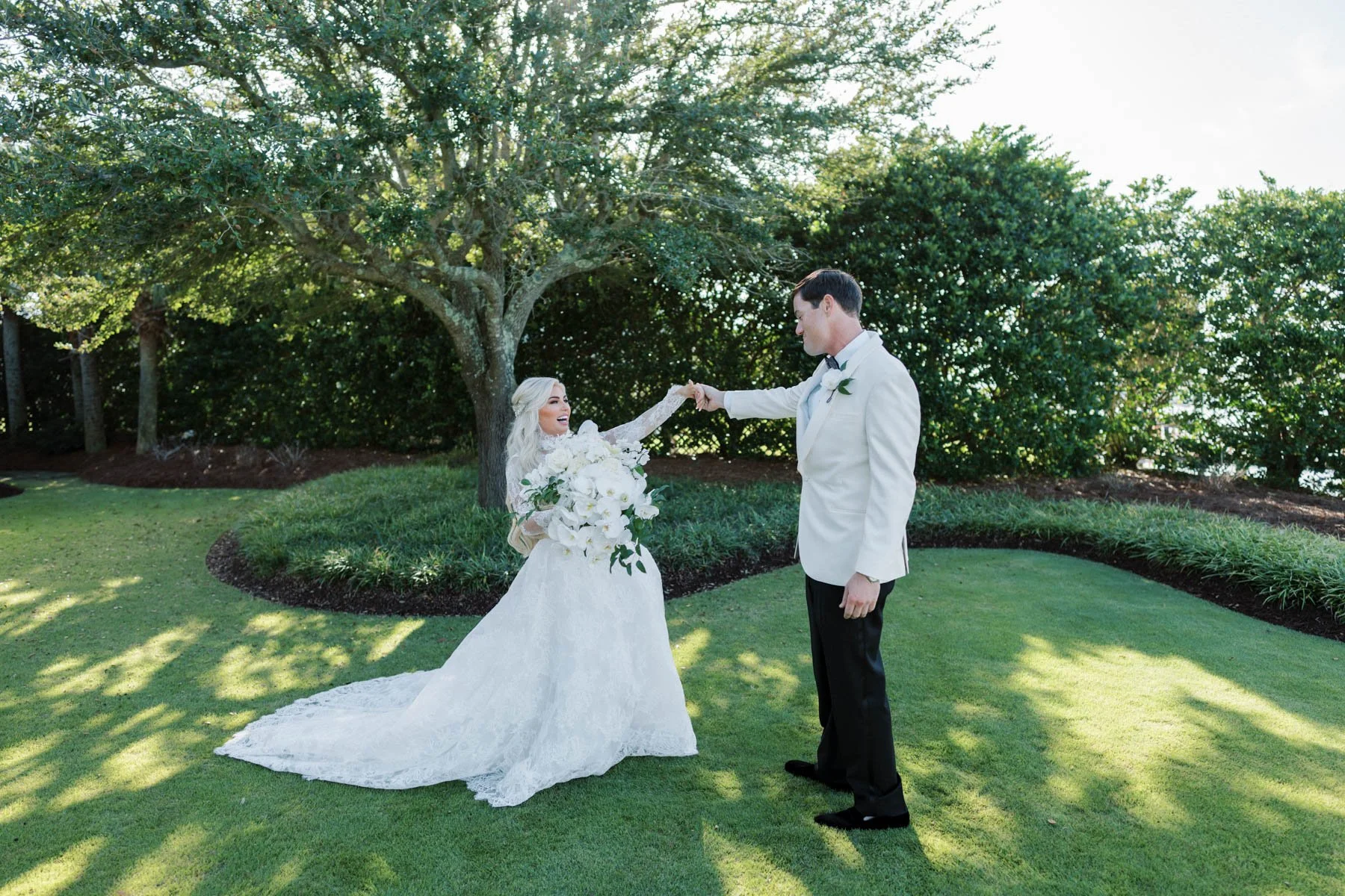 A bride and groom dancing outdoors on a green lawn with trees in the background.