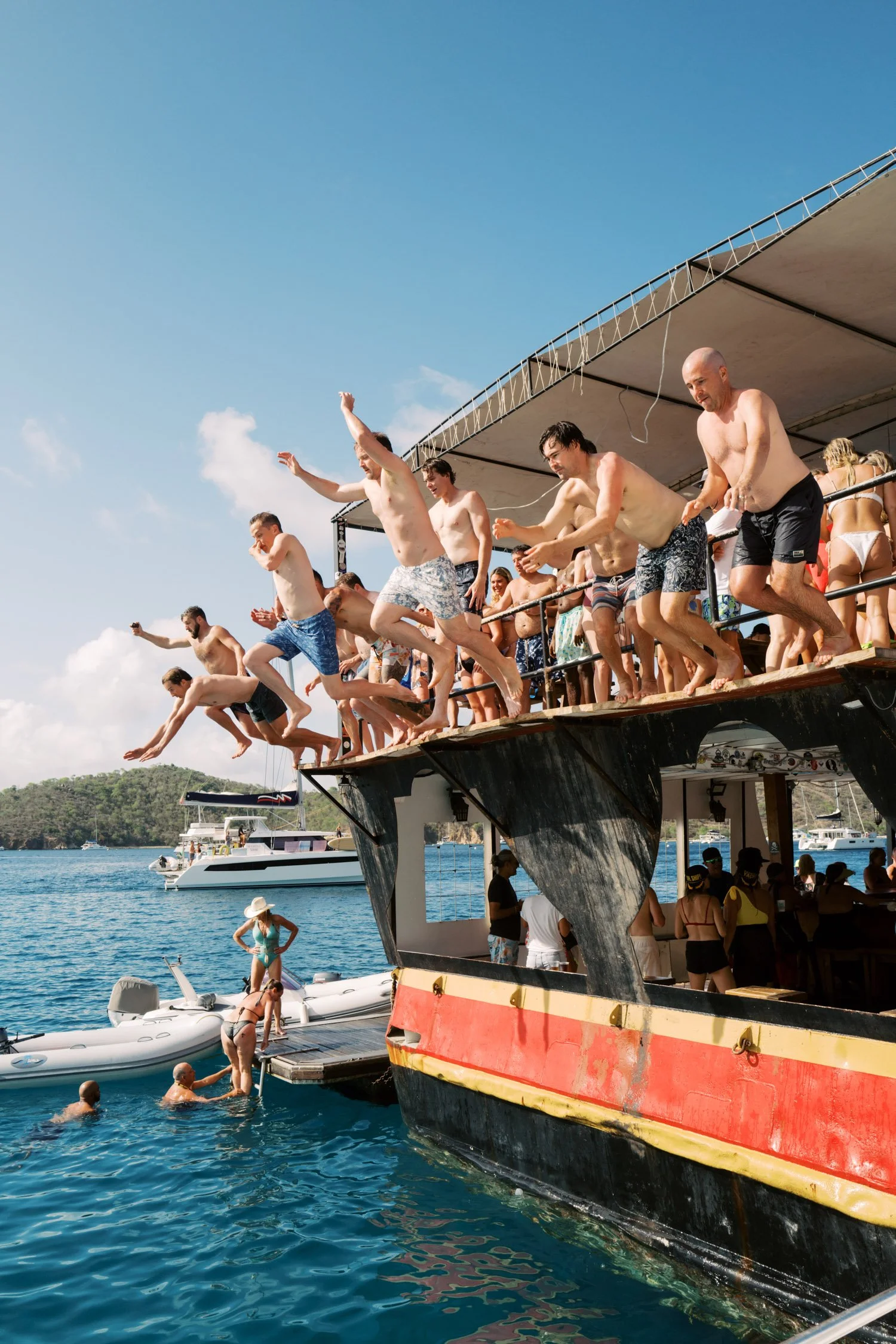 People jumping off a boat into the water at a marina on a sunny day.