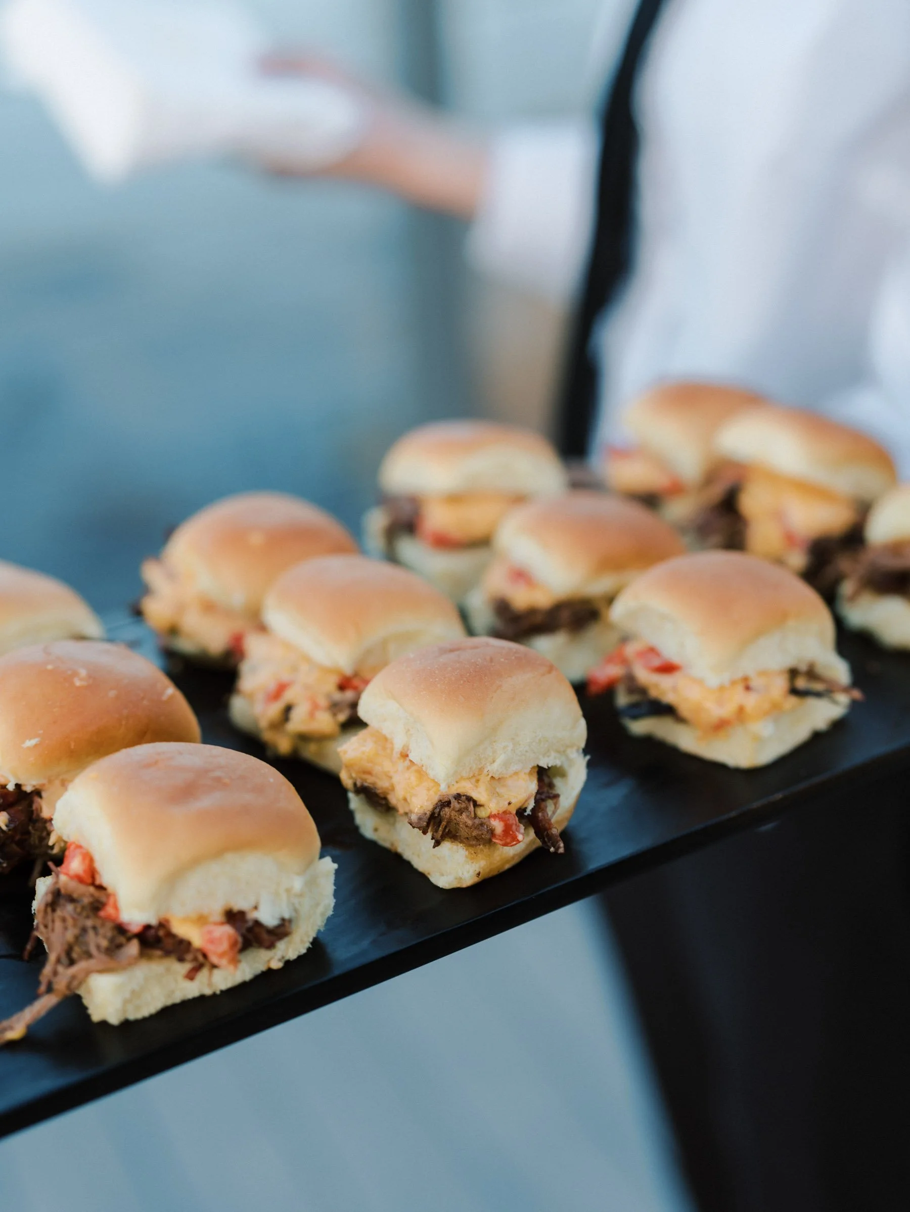Mini sandwiches with beef, chicken, and tomato fillings on a black tray.