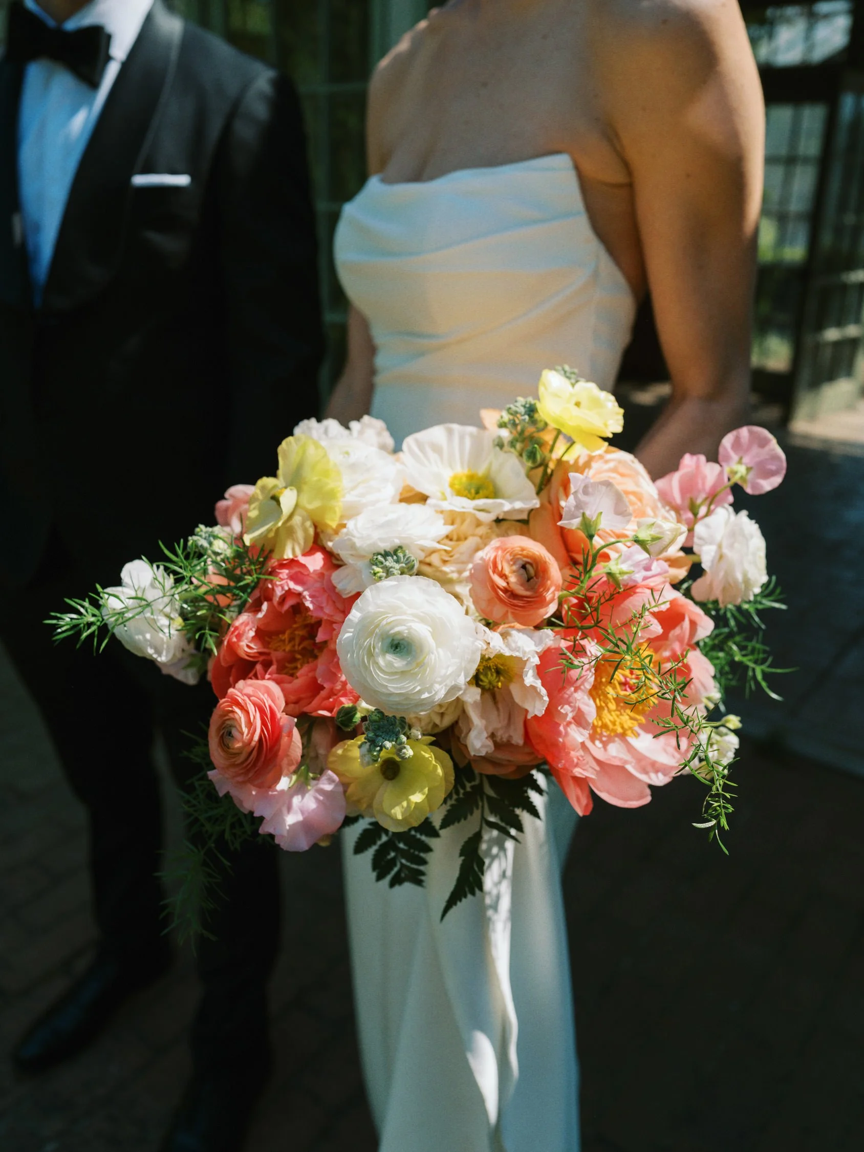 Bride in a white strapless dress holding a colorful bouquet of flowers at a wedding.