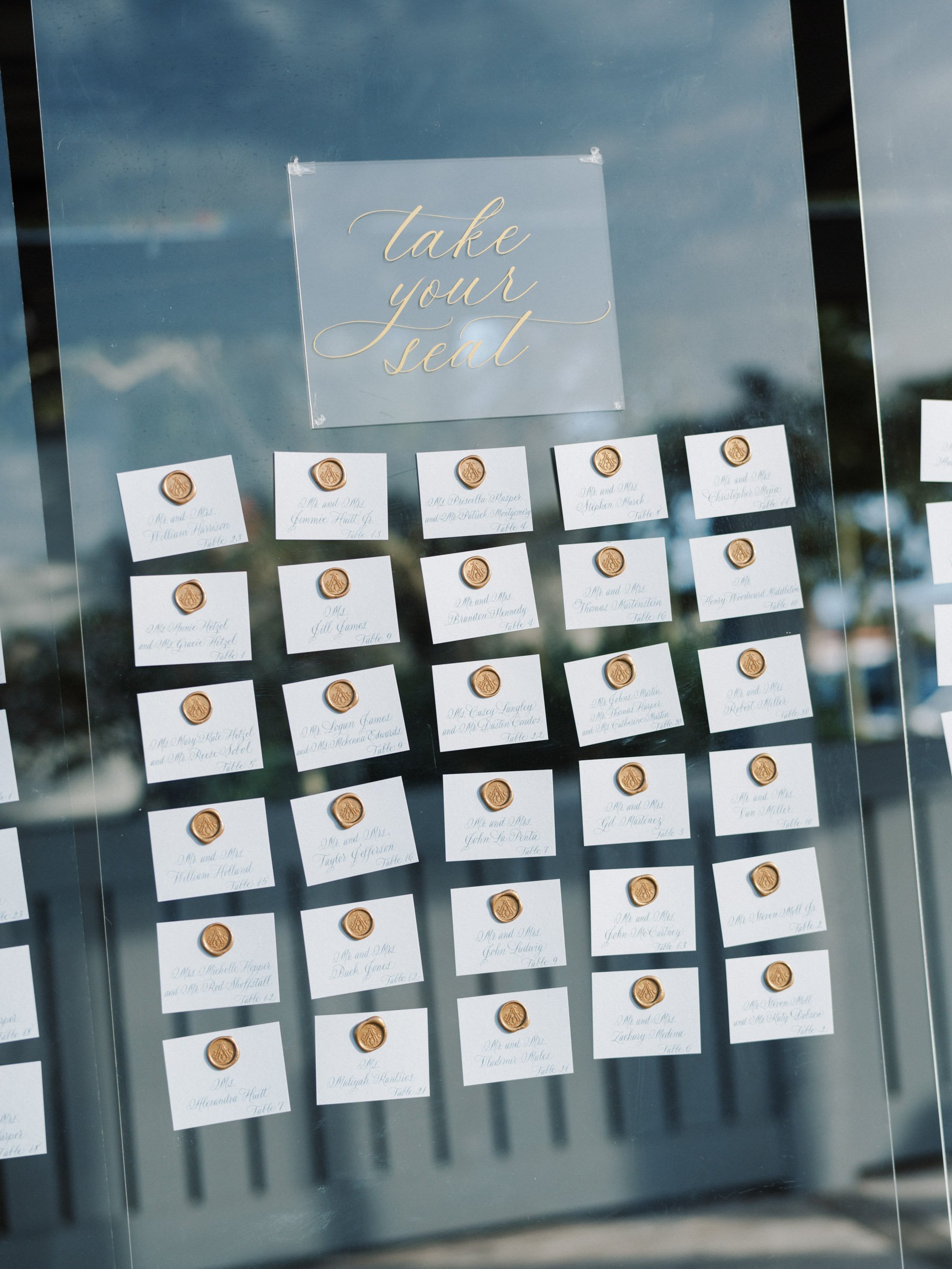 Wedding seating chart with name tags and wax seals, titled "Take your seat."