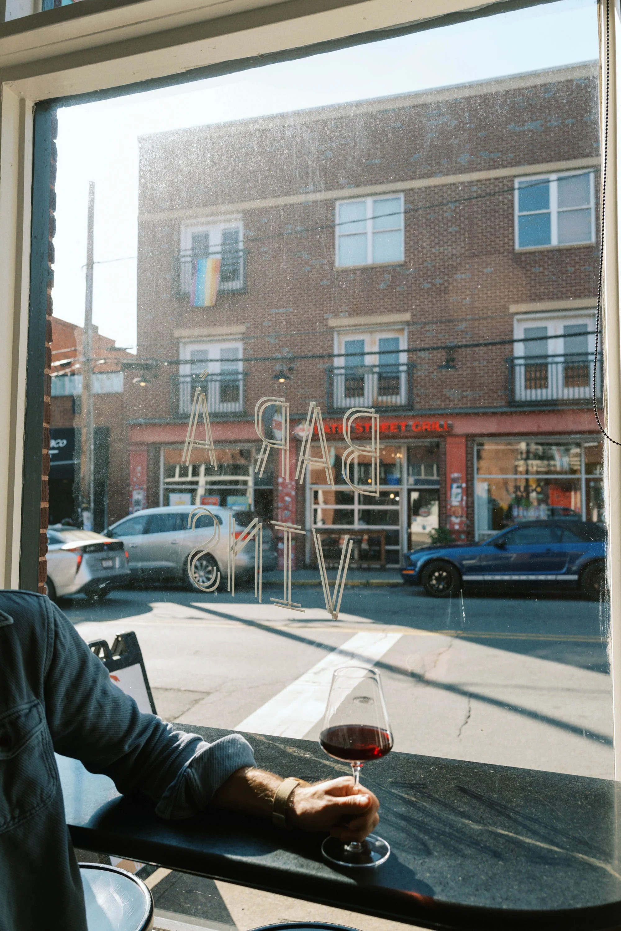 Person holding a glass of red wine sitting at a bar near a window on a city street at Bar a Vin in Noda.