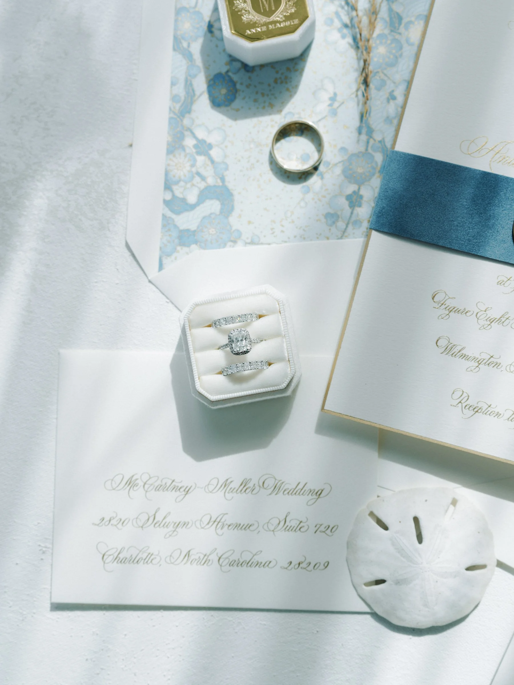 Wedding invitation, engagement ring box with diamond rings, wedding bands, and a ring box with a floral patterned interior.