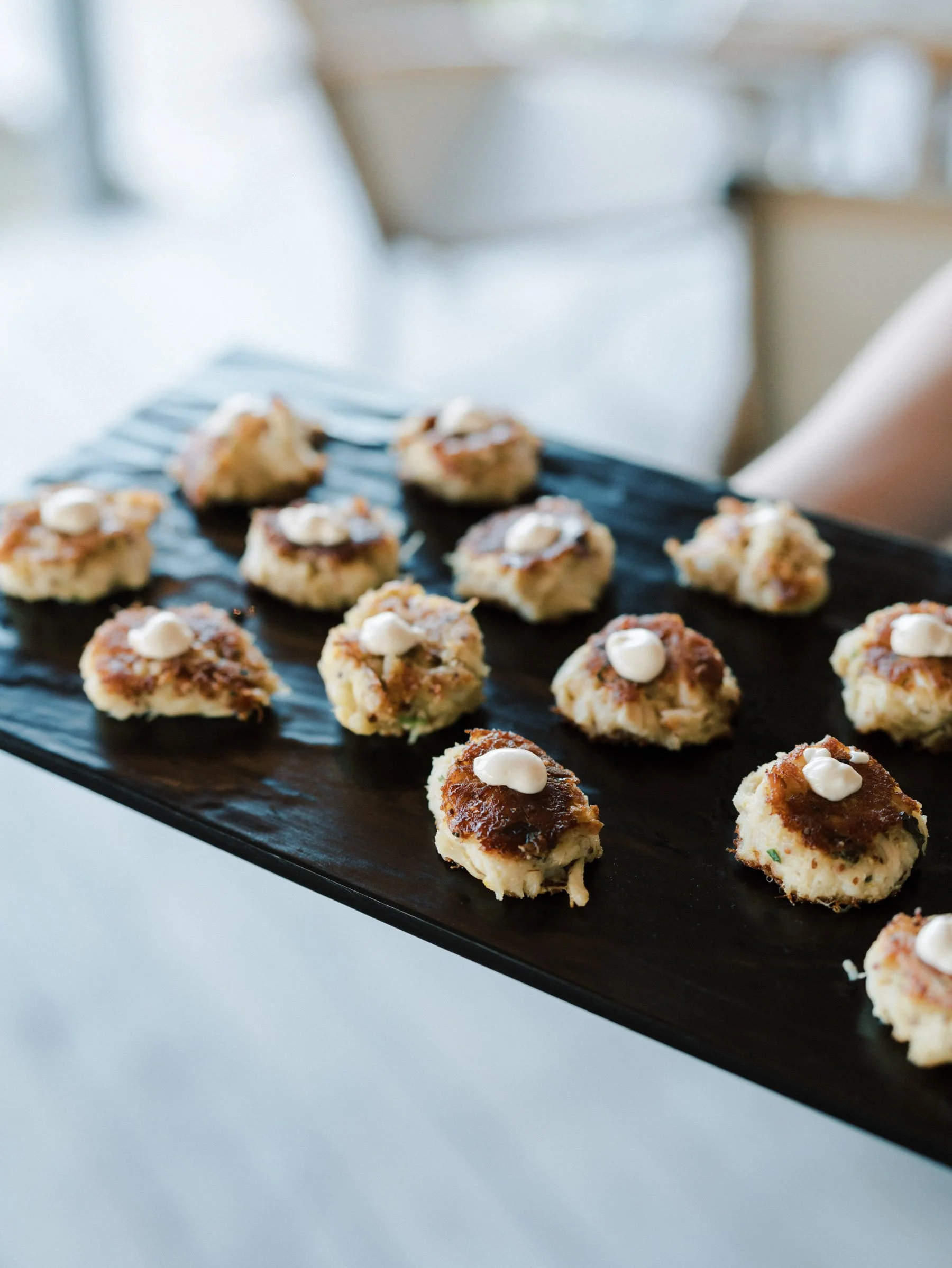 Tray of small appetizer bites topped with dollops of white sauce, served on a black tray.